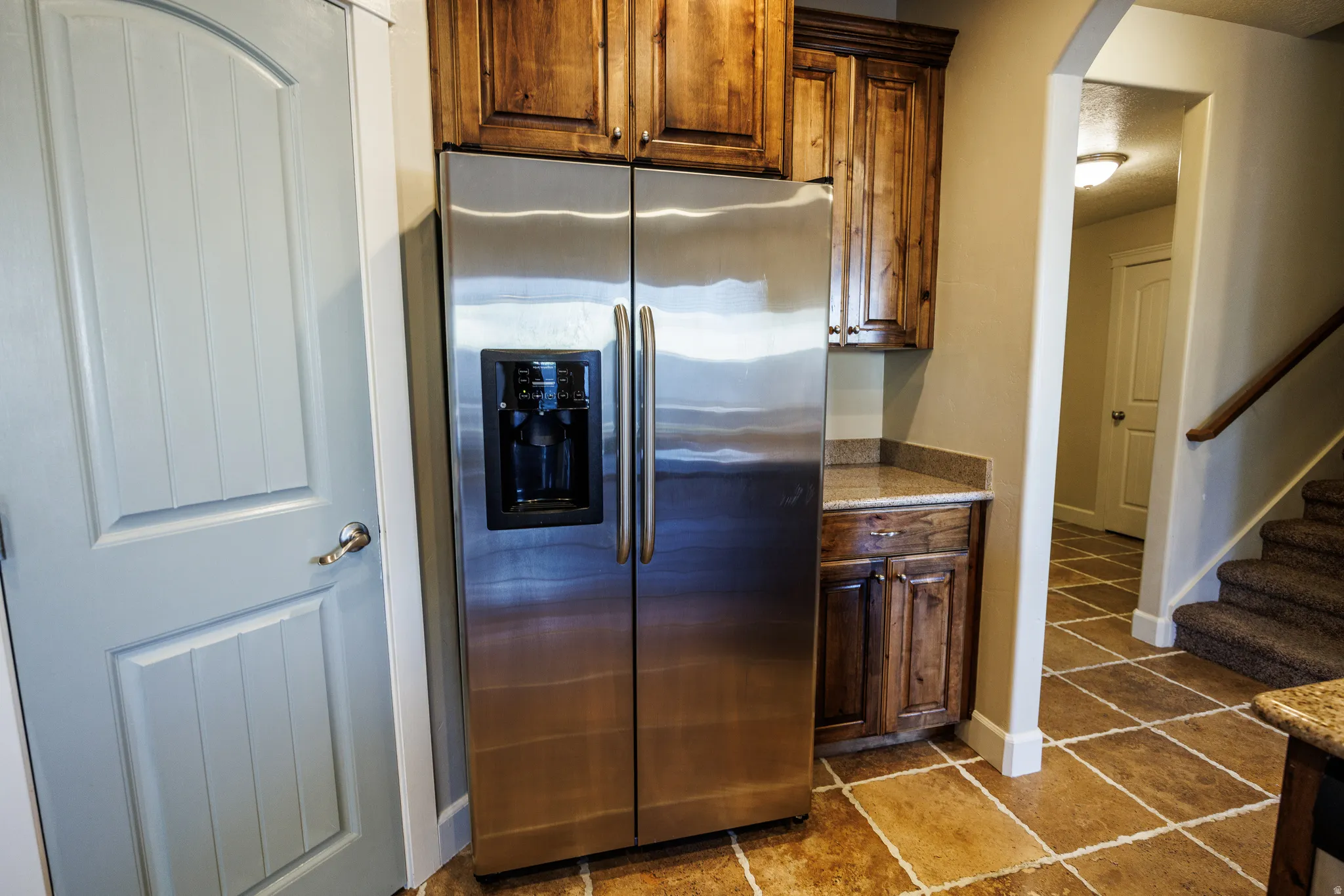 Stainless steel refrigerator with a built-in dispenser, surrounded by custom wood cabinetry and granite countertops