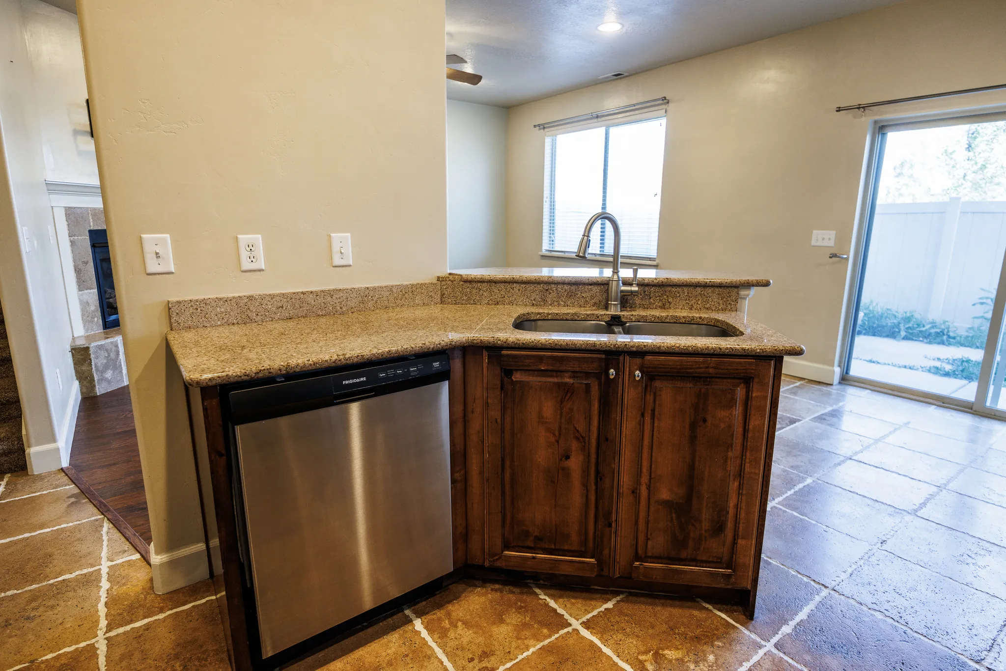 Kitchen island featuring a double basin sink with a high-arc faucet, stainless steel dishwasher, wood-finish cabinetry, and a granite-style countertop