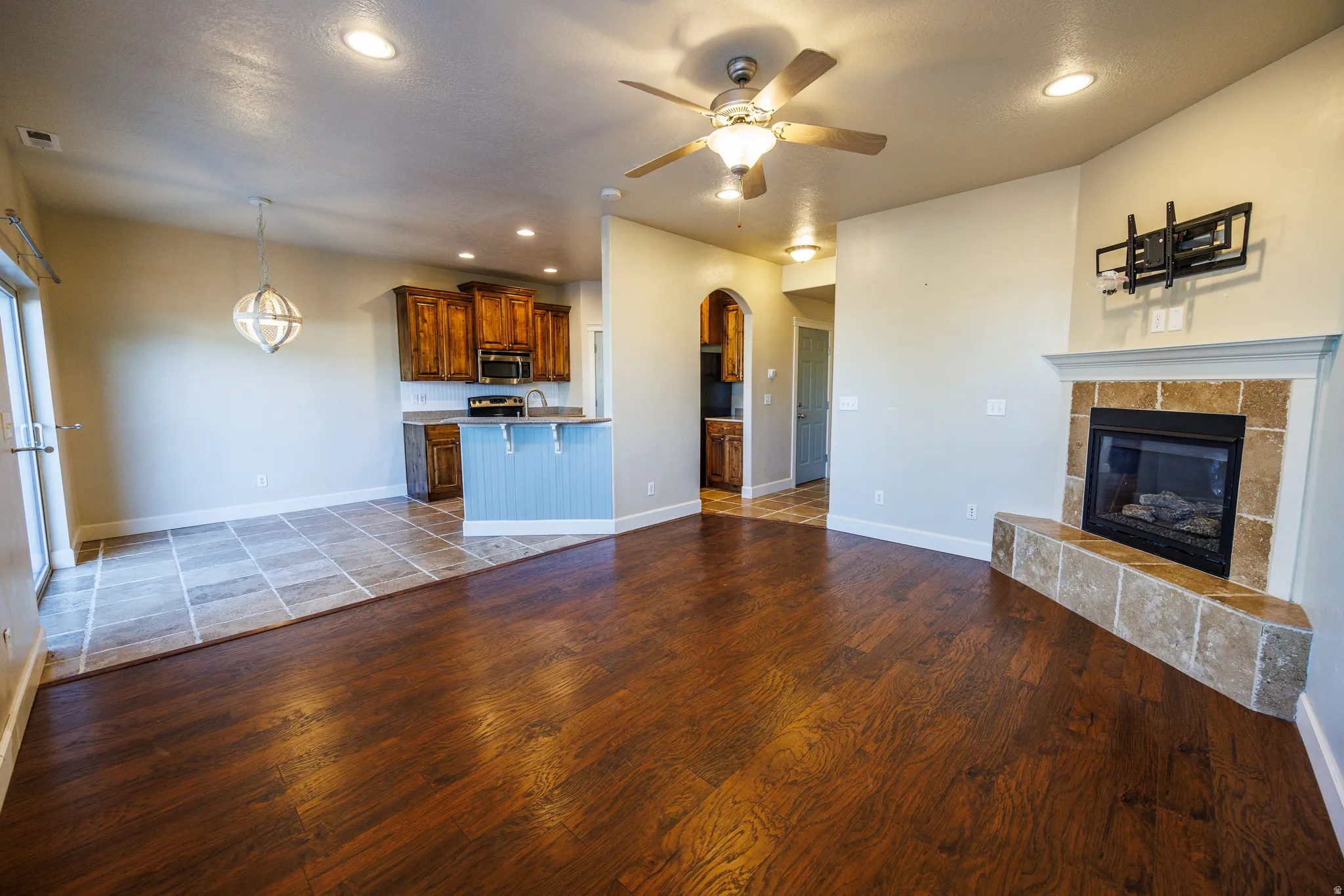 Spacious living area featuring wood-finish flooring, a corner fireplace with stone surround and hearth, and a ceiling fan