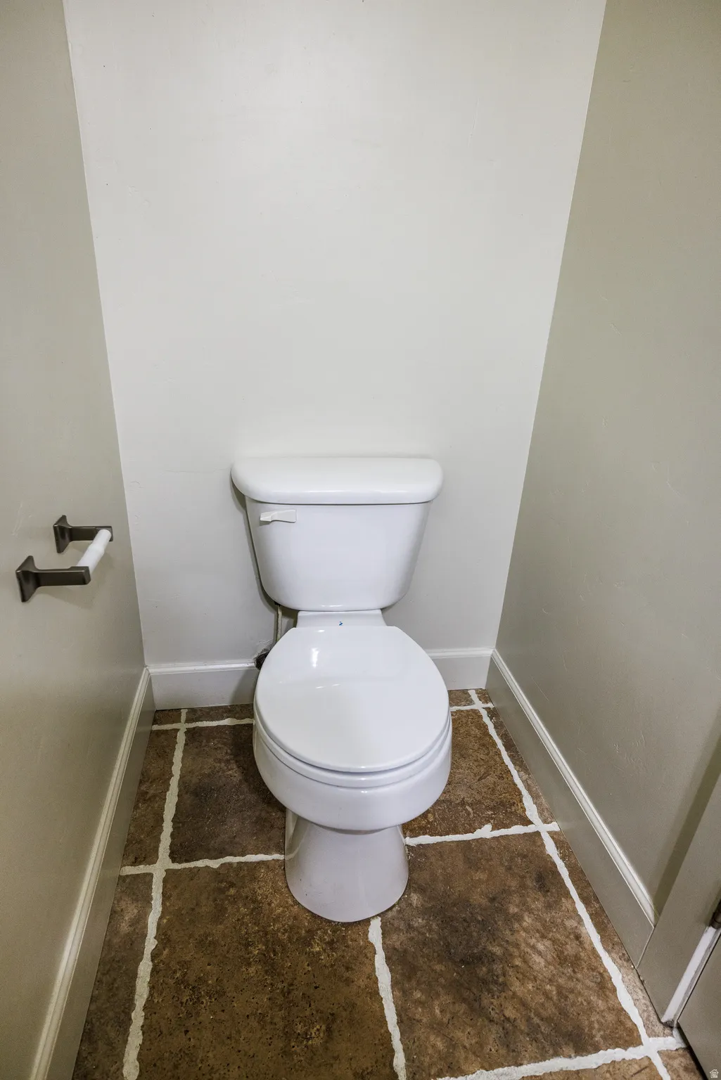 White toilet with a round bowl, set against light-colored walls and a brown tile floor with white grout