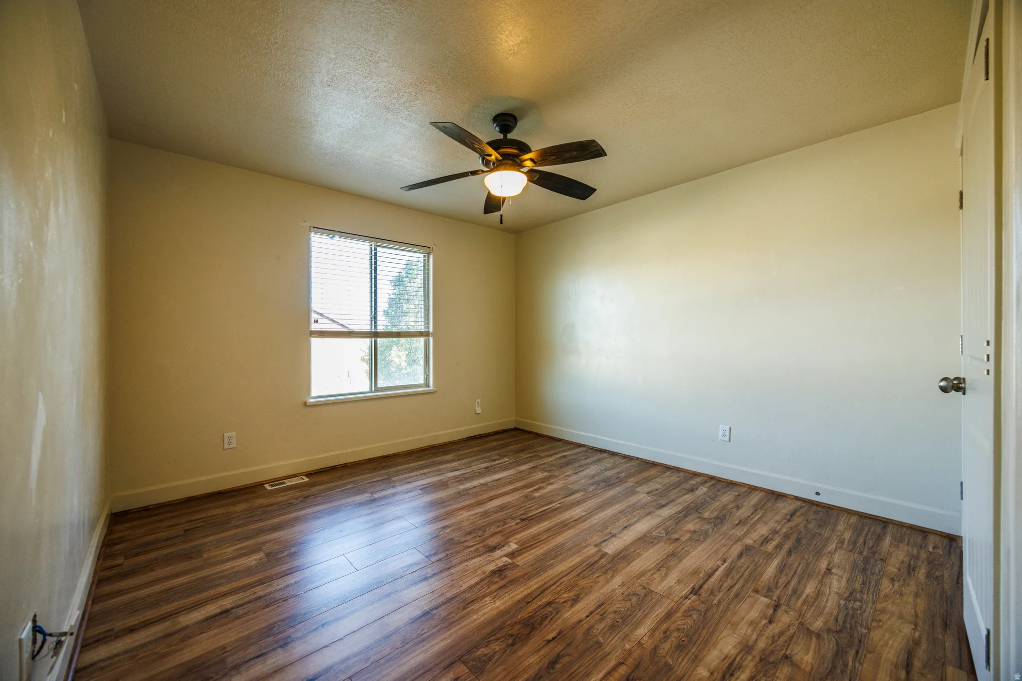 Spacious room featuring wood-finish flooring, a window with blinds, and a ceiling fan with integrated lighting