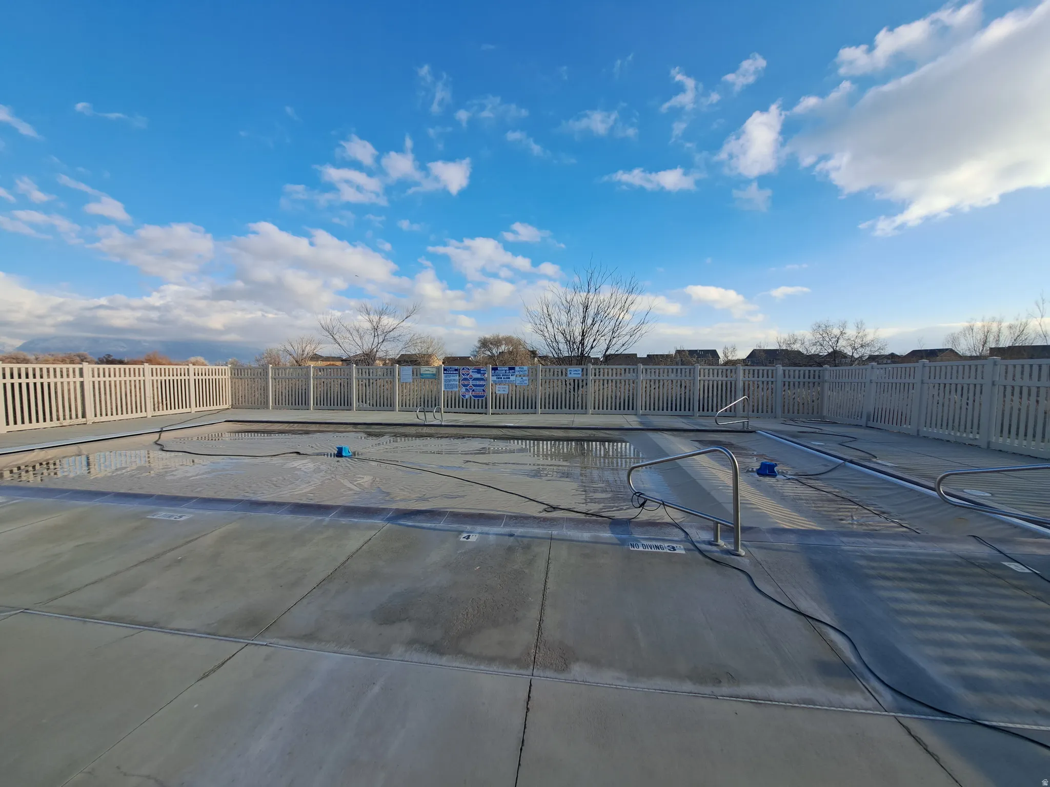Outdoor pool area featuring concrete decking, a perimeter fence with vertical slats, and integrated pool cover systems