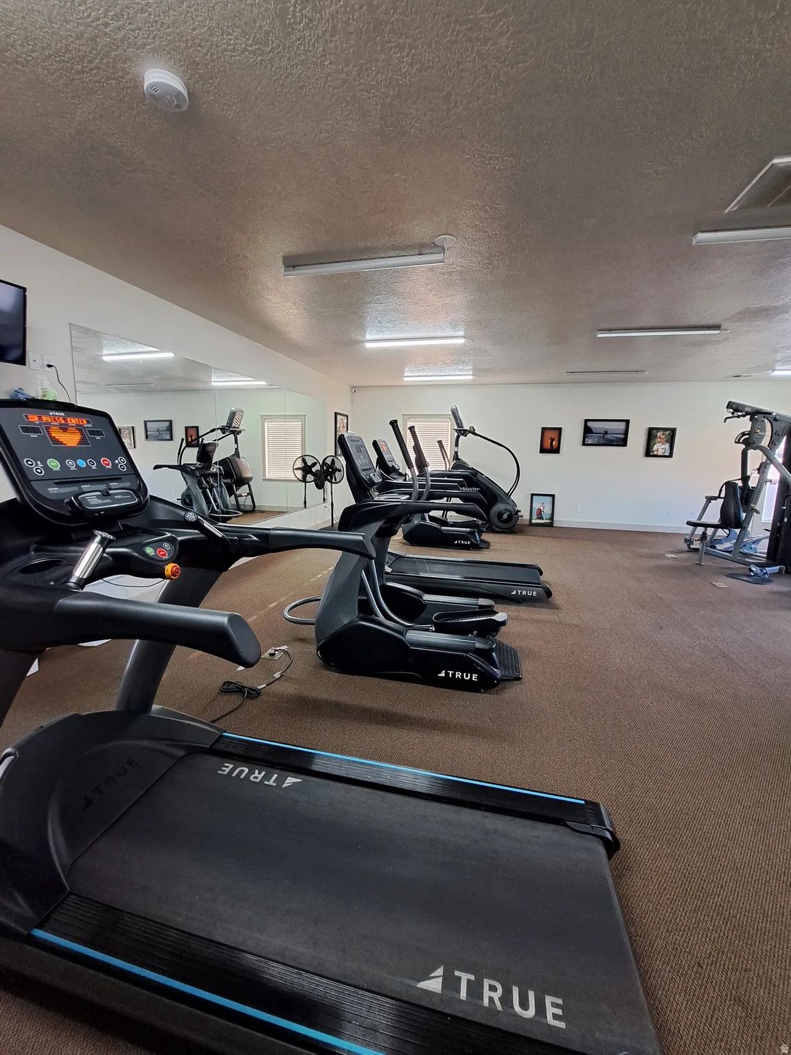 Fitness room featuring multiple cardio machines, wall-mounted mirrors, recessed lighting, and durable carpet flooring