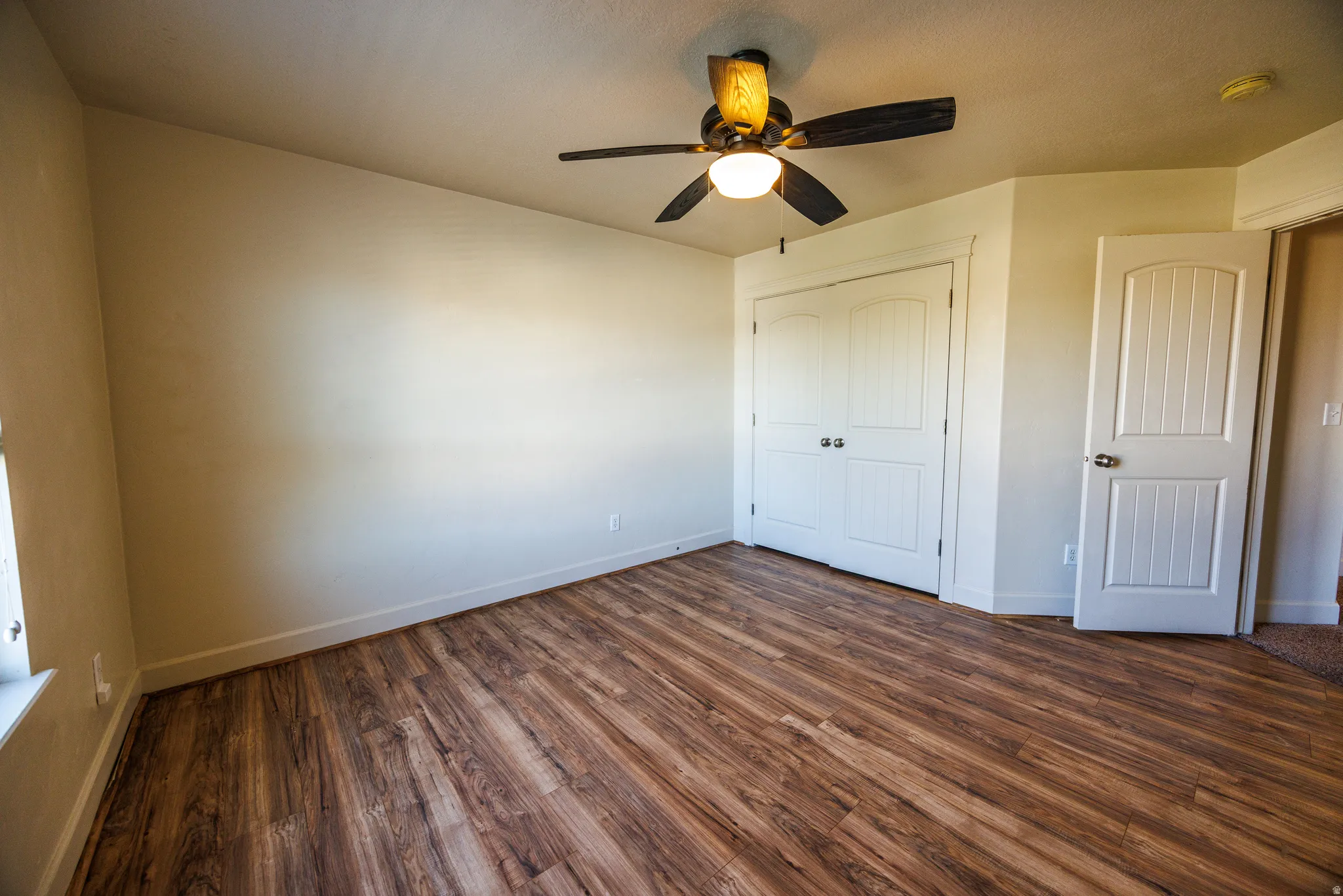 Room featuring wood-finish flooring, a ceiling fan with integrated lighting, and white baseboards