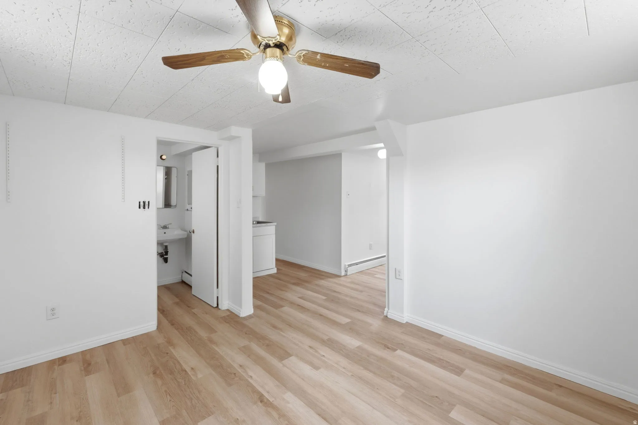 Open living area featuring wood-finish flooring, white baseboards, and a ceiling fan with light fixture