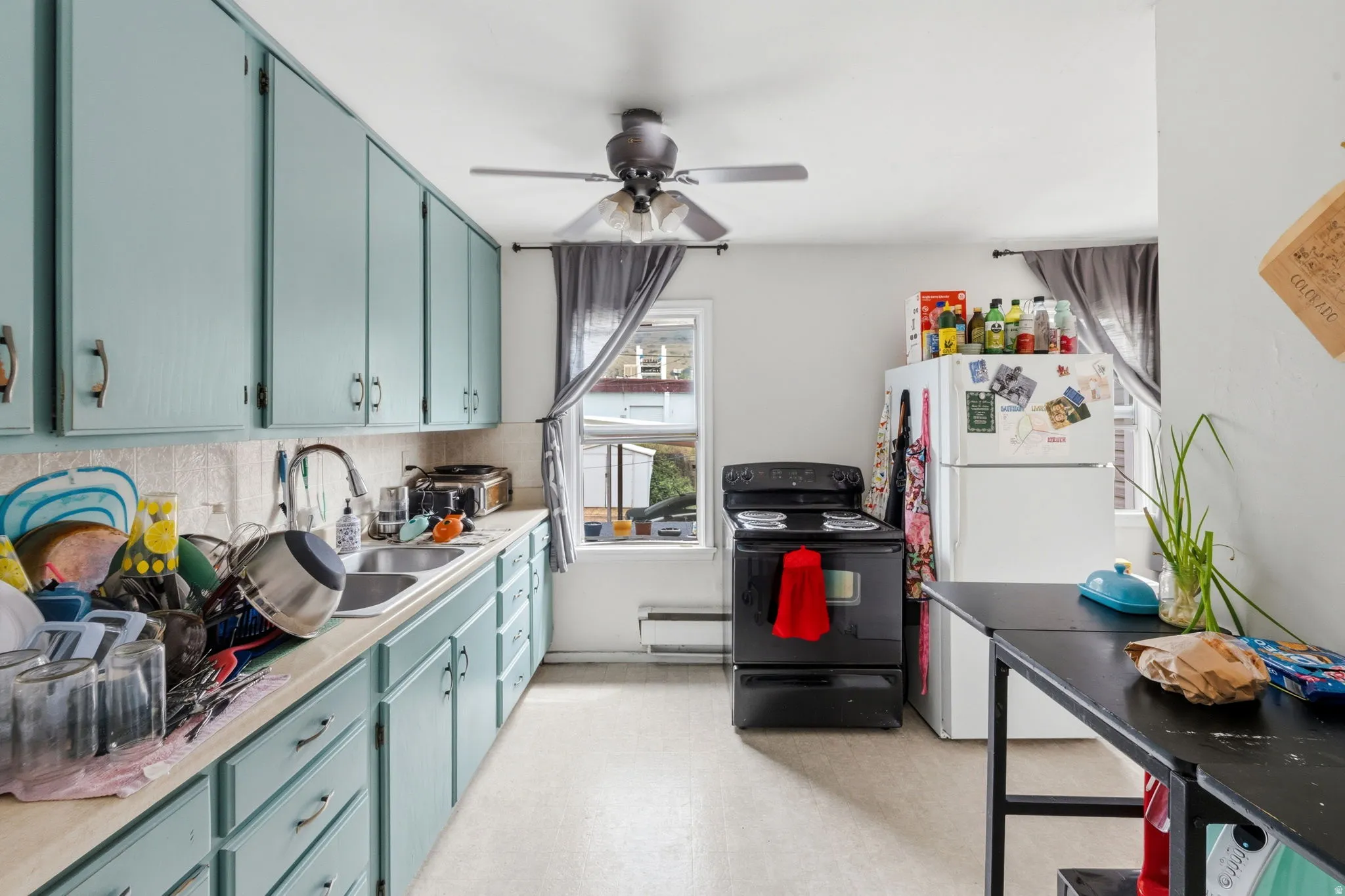 Kitchen featuring light blue cabinetry, light-toned countertops, a dual-basin stainless steel sink, and a ceiling fan with integrated lighting