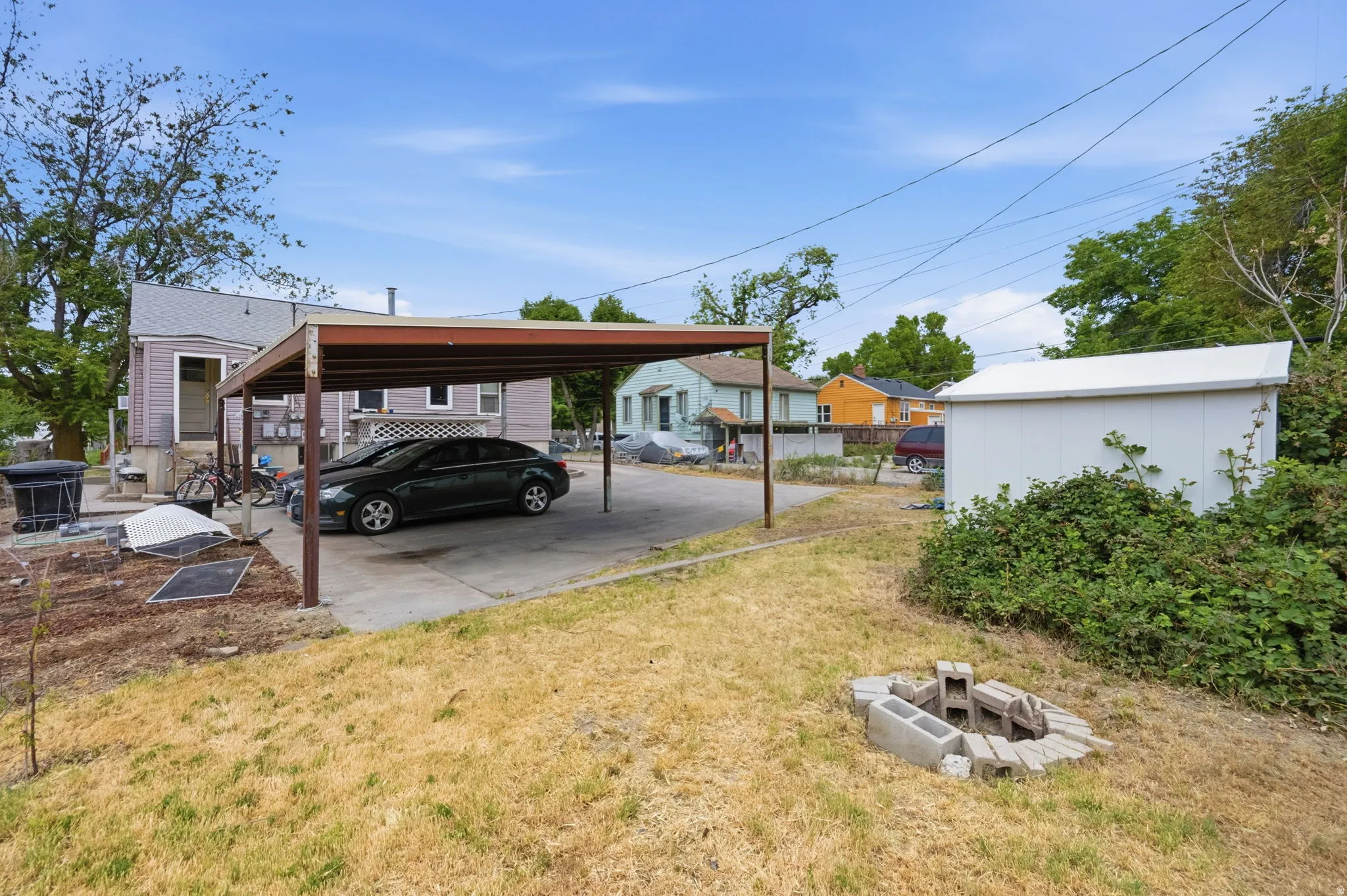 Expansive backyard featuring a concrete patio, metal carport, and a white storage shed
