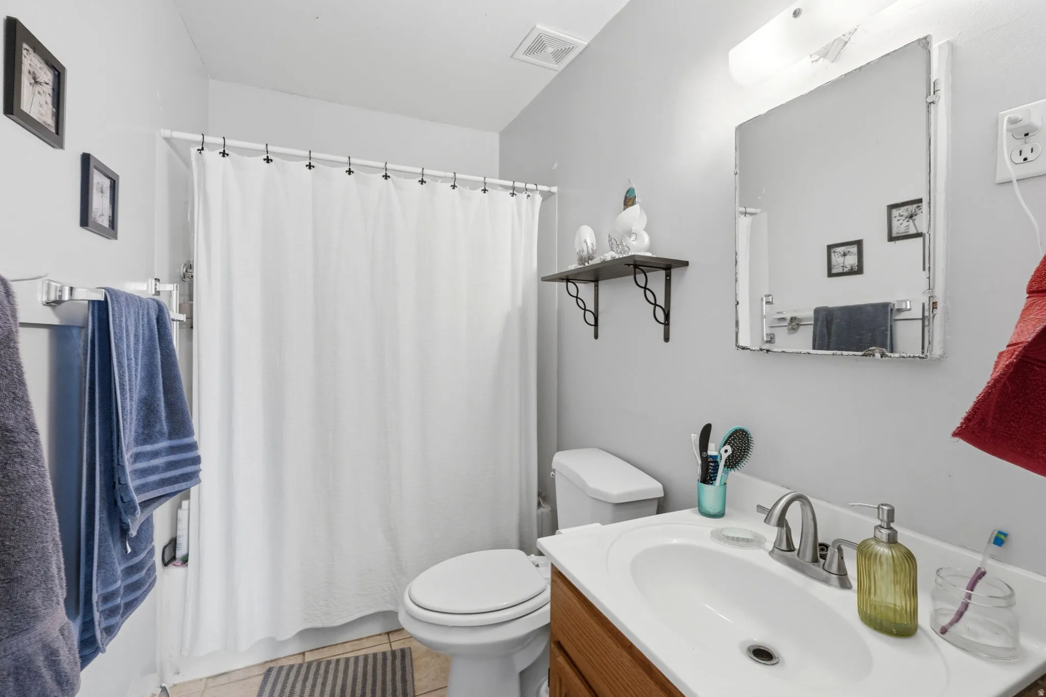 Bathroom featuring light gray walls, tile flooring, a built-in wooden vanity with a white countertop and integrated sink, a toilet, and a shower with a white curtain
