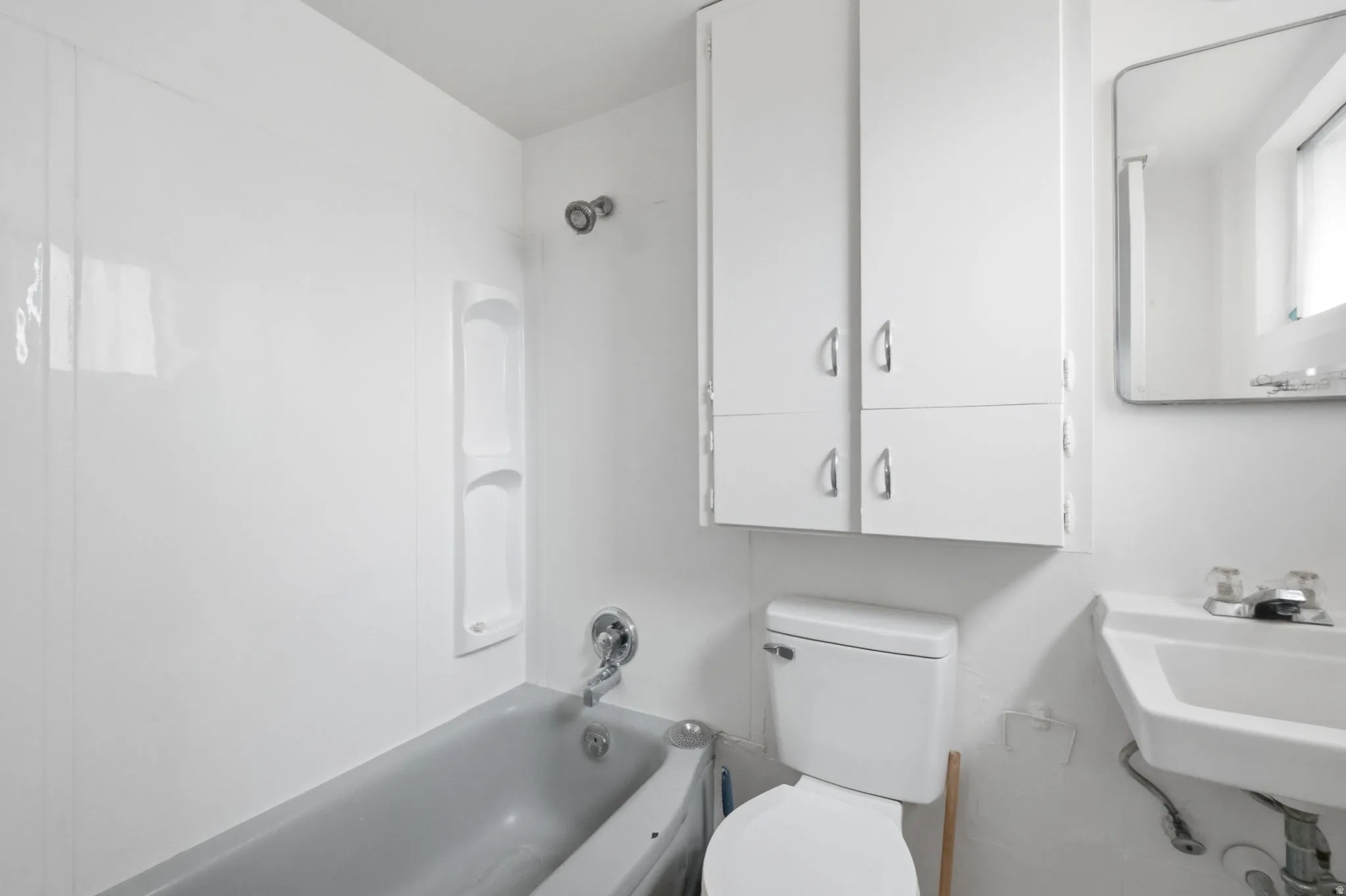 Bathroom featuring a white wall-mounted sink, a toilet, and a bathtub with white surround panels