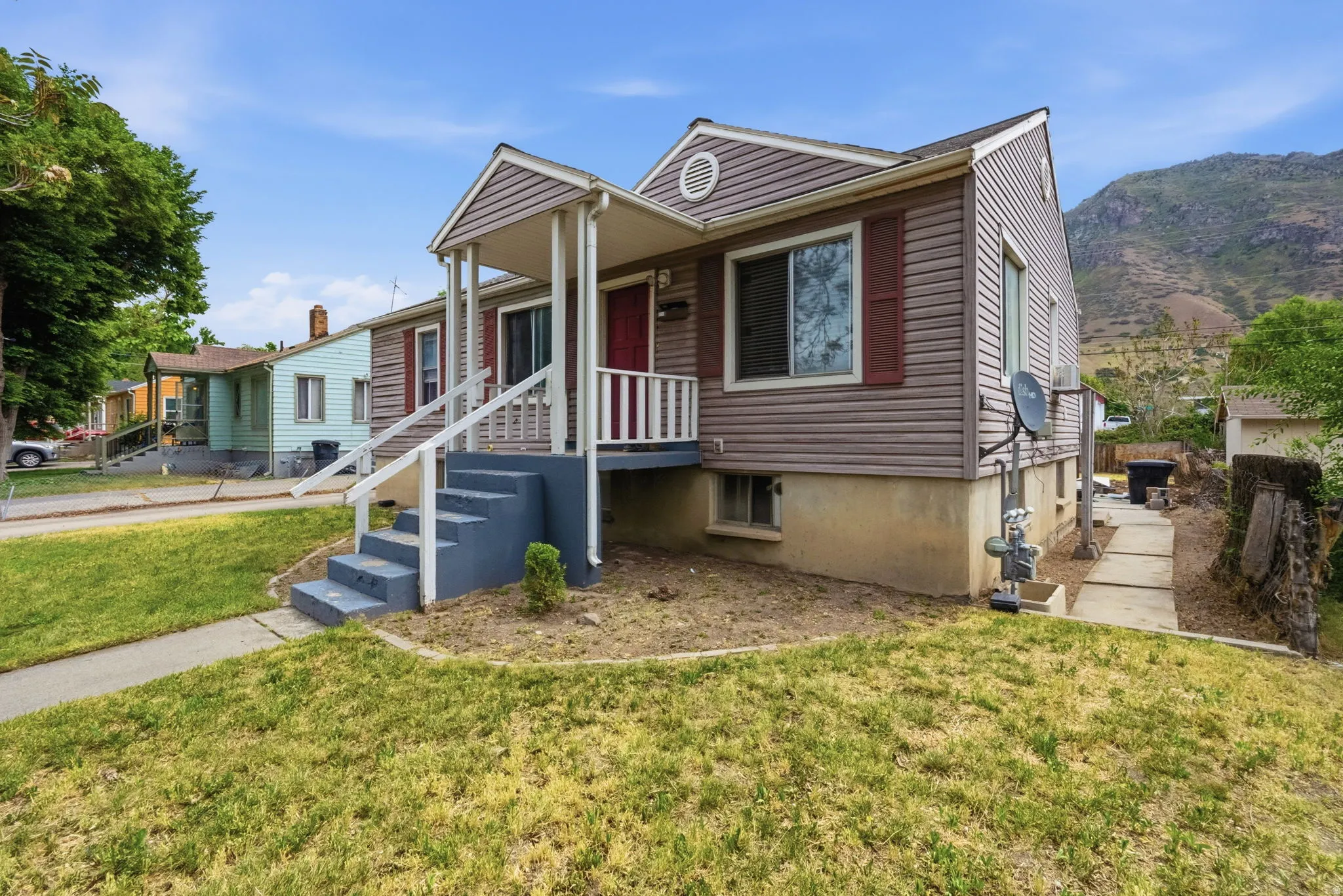 Vinyl-sided home featuring a covered front porch with white railings, a red entry door, and dark red window shutters