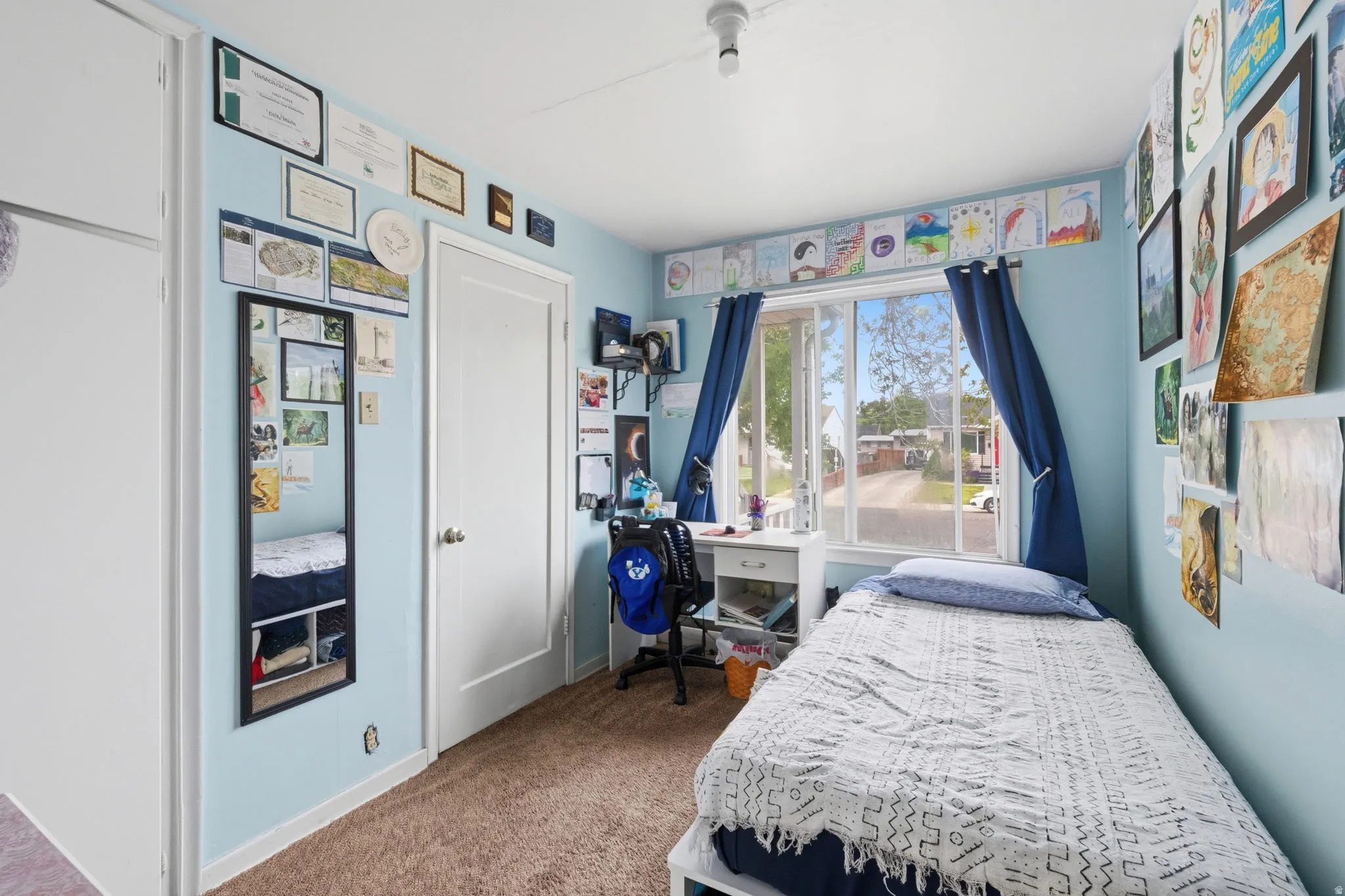 Room featuring a large window with white trim, light blue painted walls, and brown carpet flooring