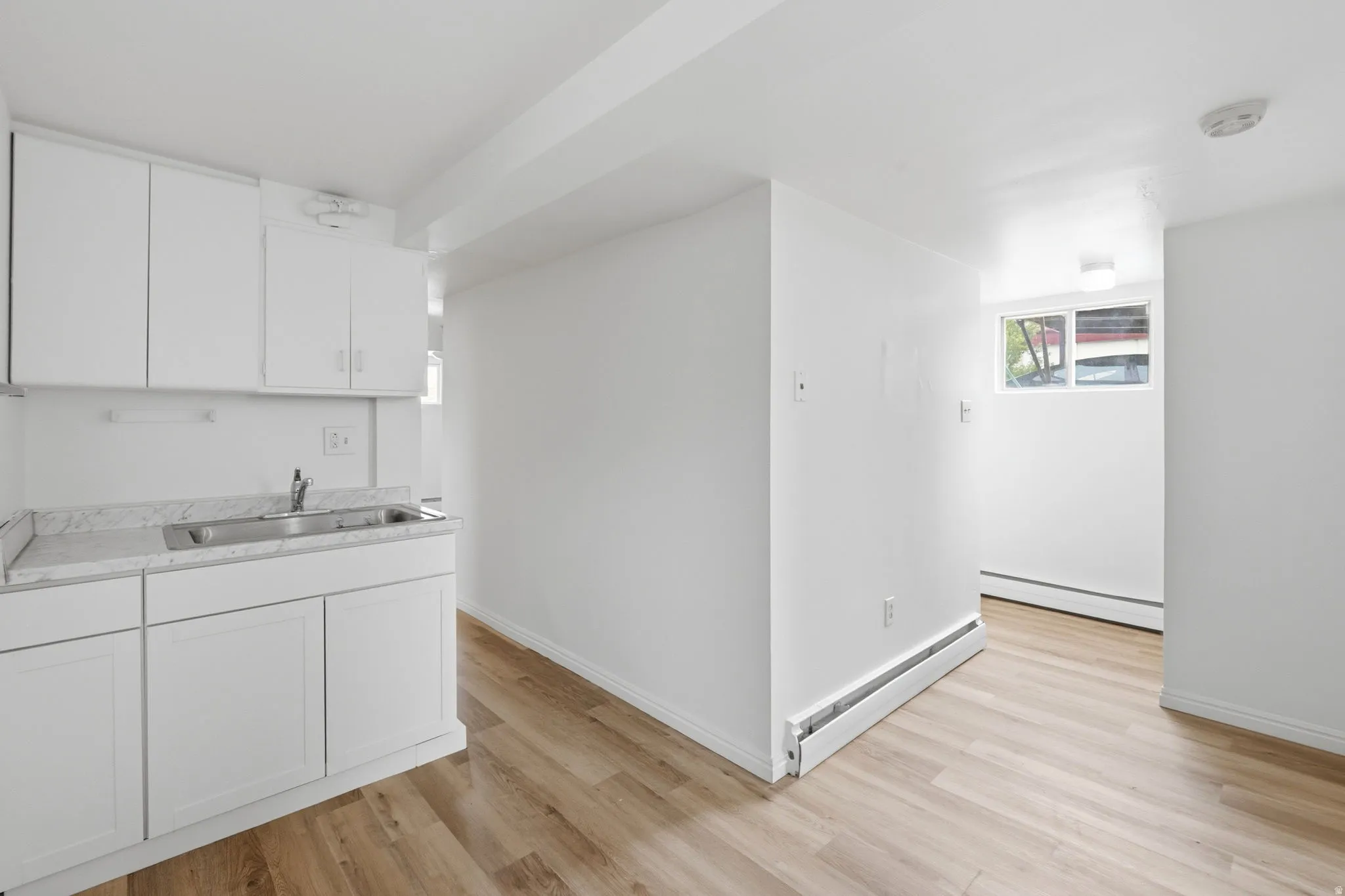 Compact kitchen area featuring white cabinetry, a double basin stainless steel sink, and light-toned countertops