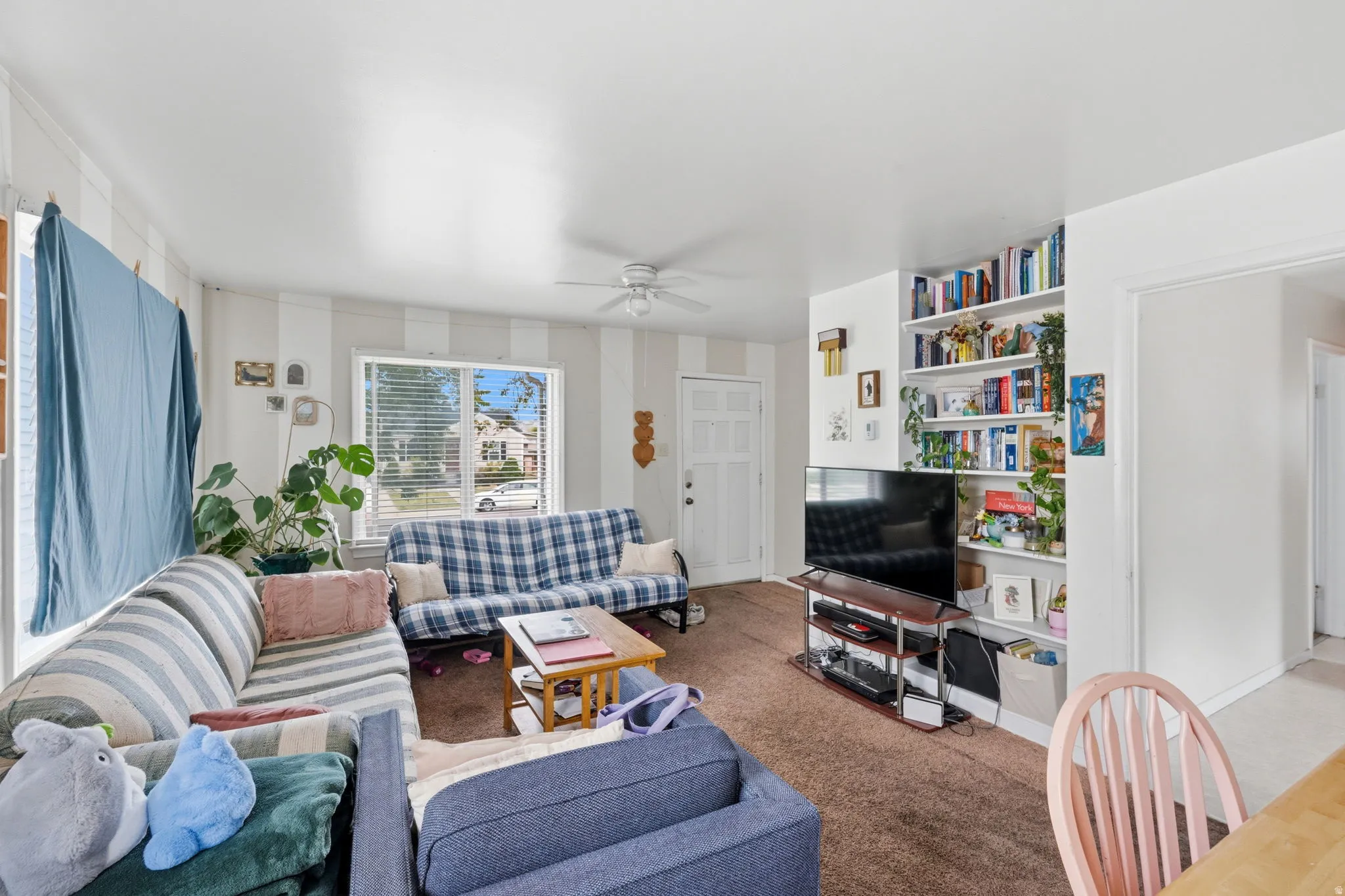 Living area featuring light-toned walls with vertical stripes, a prominent window with blinds, and brown carpet flooring