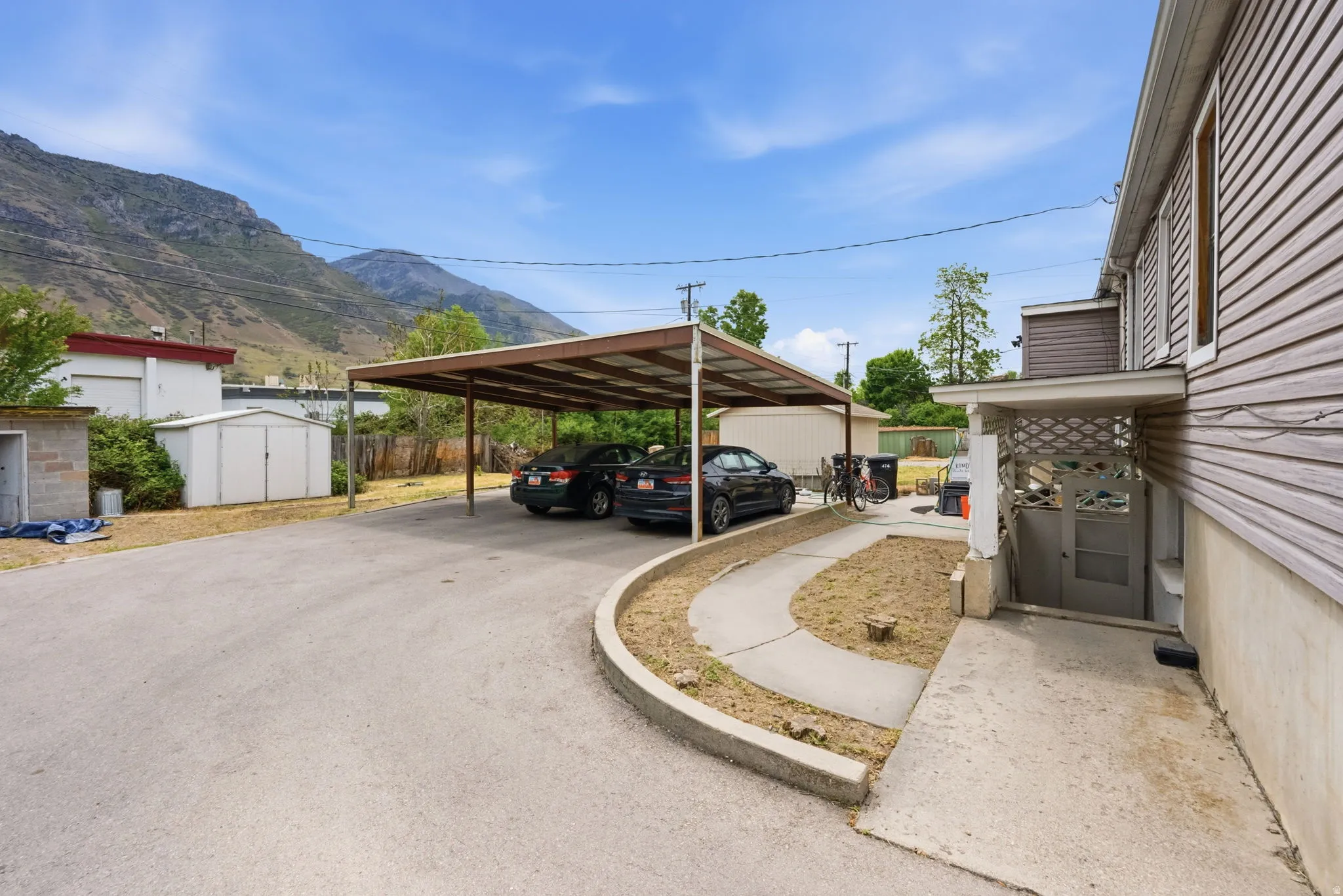 Expansive paved driveway offering a multi-vehicle carport, an additional detached storage shed, and a concrete side pathway