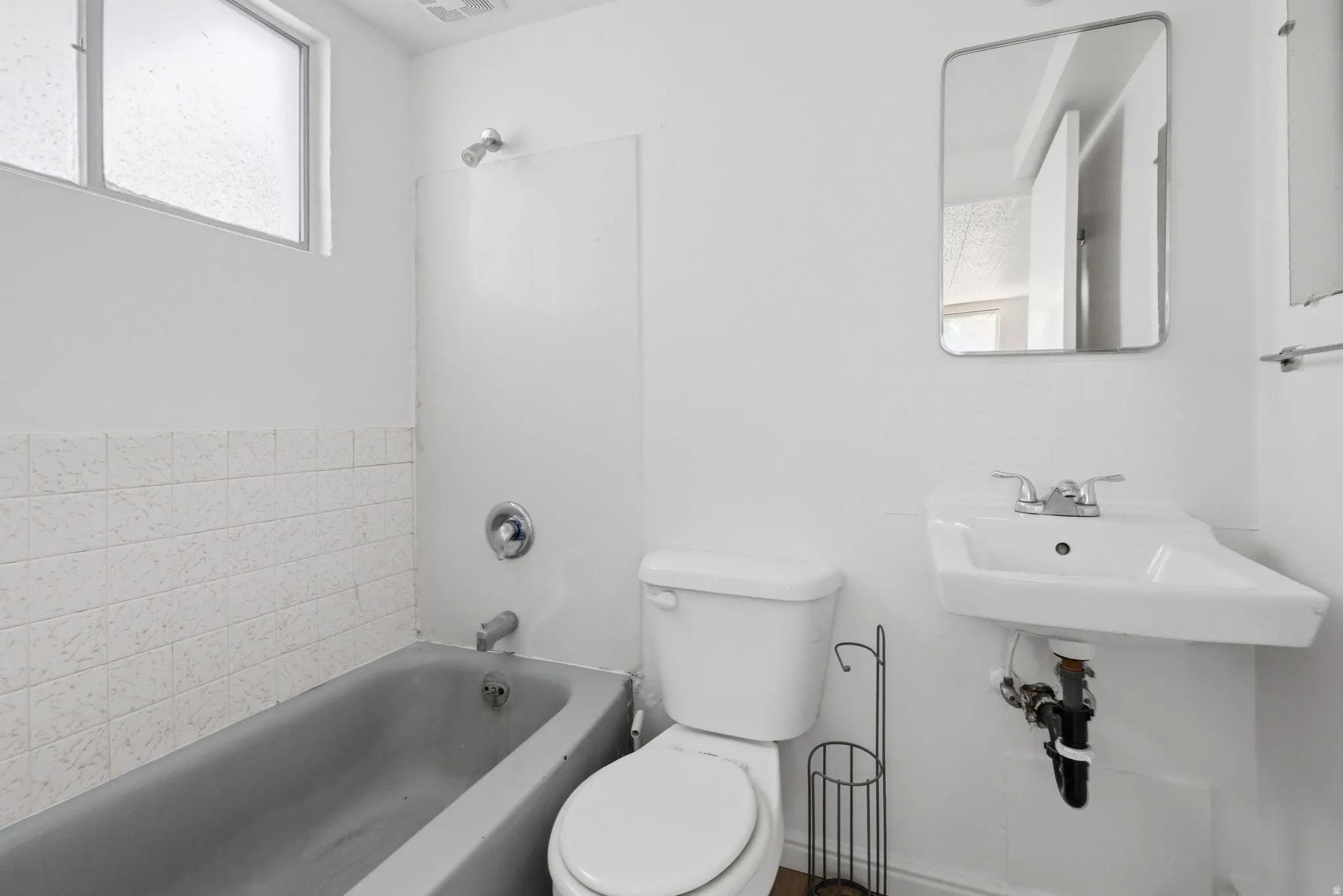 Bathroom featuring a wall-mounted sink, toilet, and bathtub with shower fixture