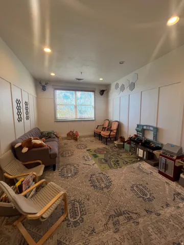 Recessed lighting illuminating a room featuring wainscoting paneling, a large window, and patterned area rugs