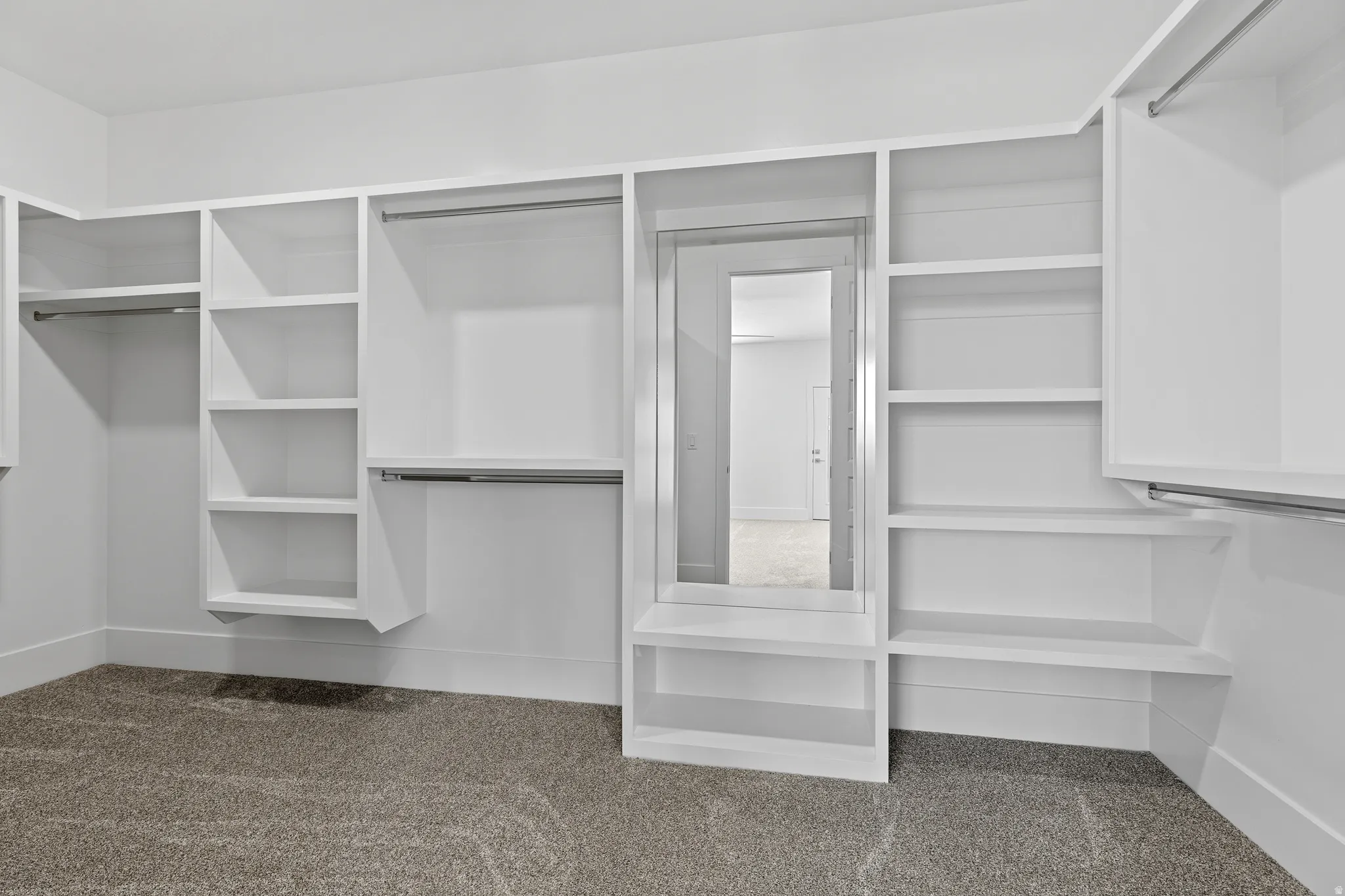 Built-in white cabinetry featuring multiple shelving units, hanging rods, and a full-length mirror