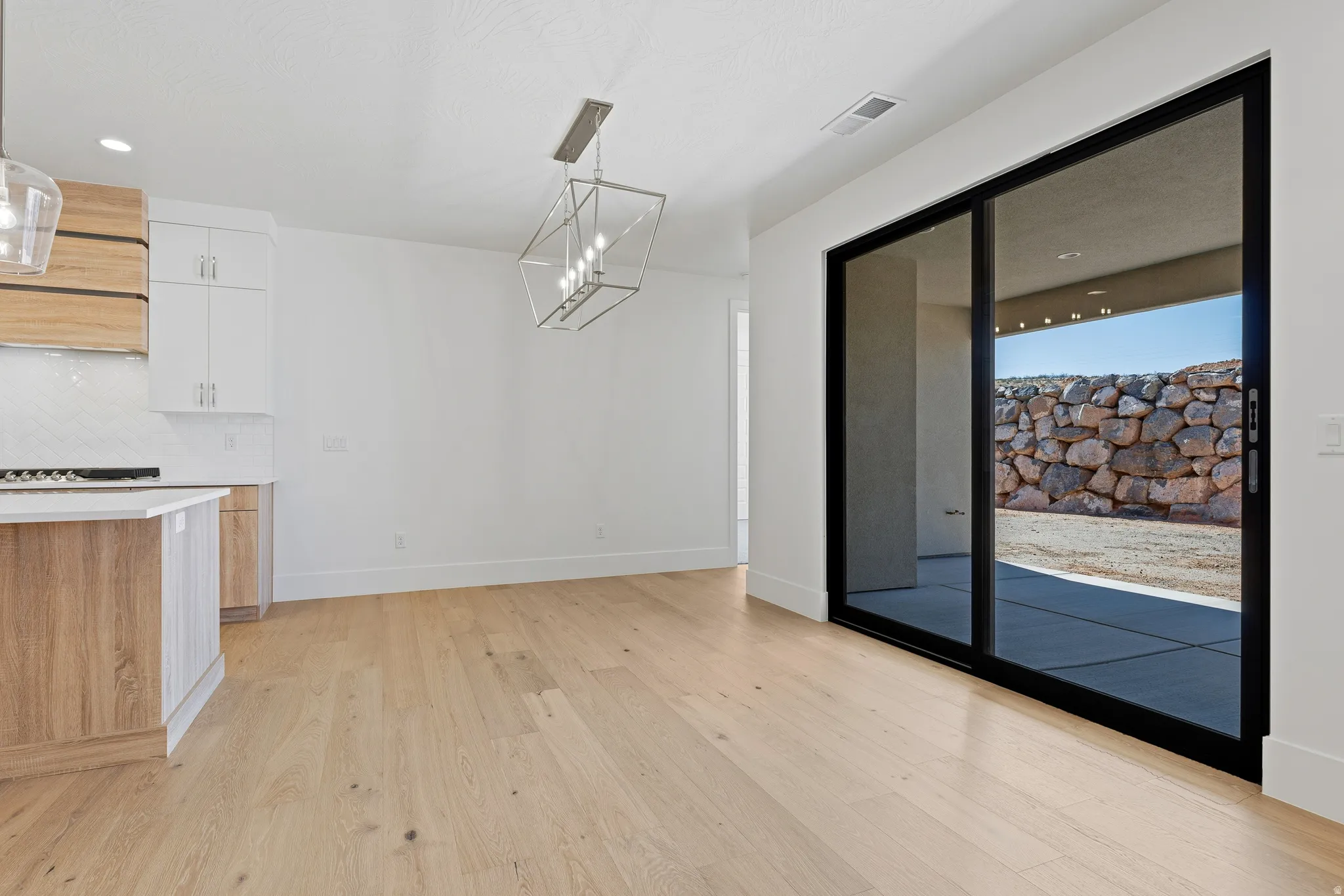 Spacious open-concept room featuring light wood-finish flooring and a contemporary linear chandelier