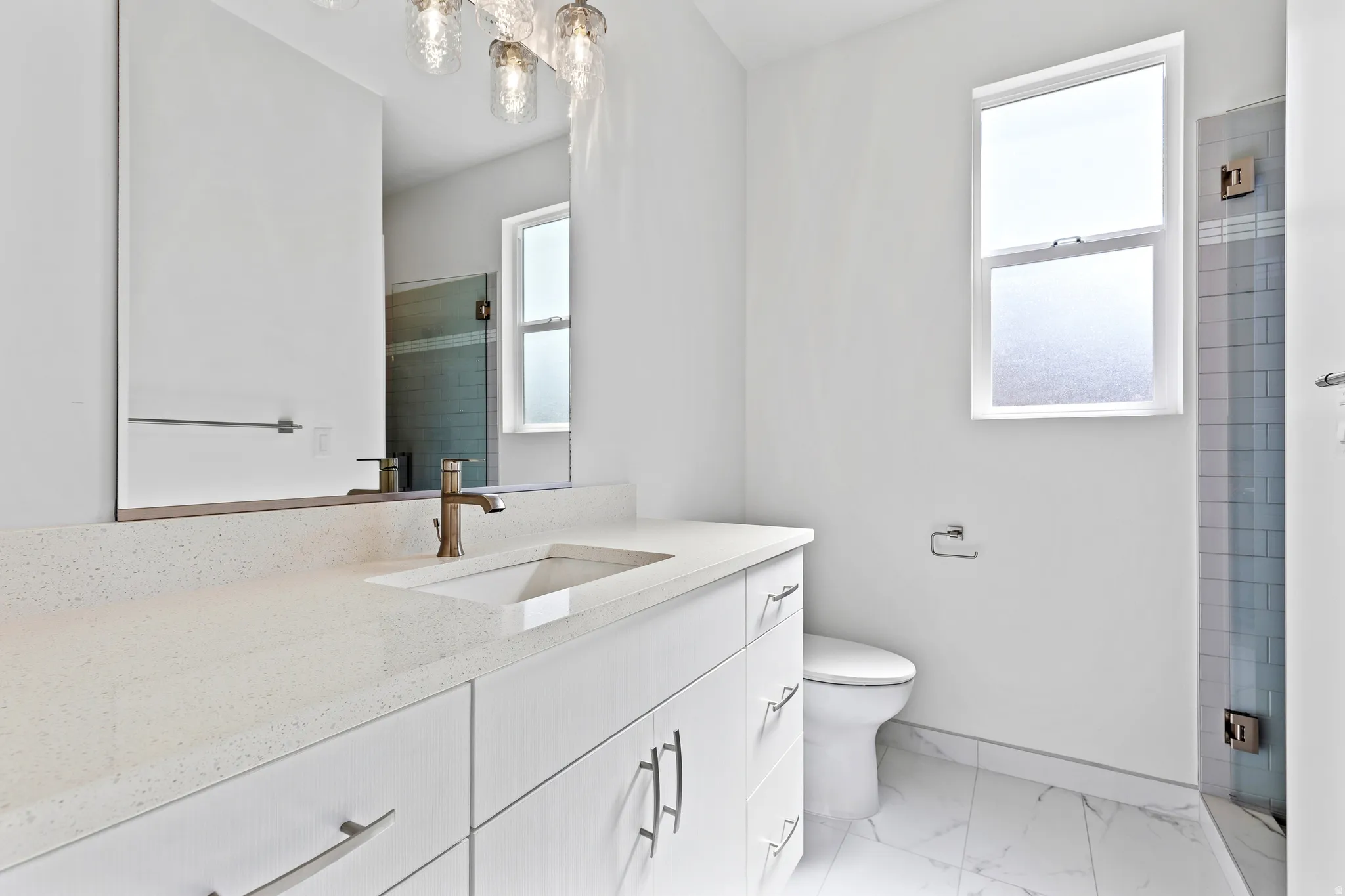 Bright bathroom featuring a spacious vanity with an integrated sink, a large mirror, a separate glass-enclosed shower, a frosted window, and marble-look floor tiles