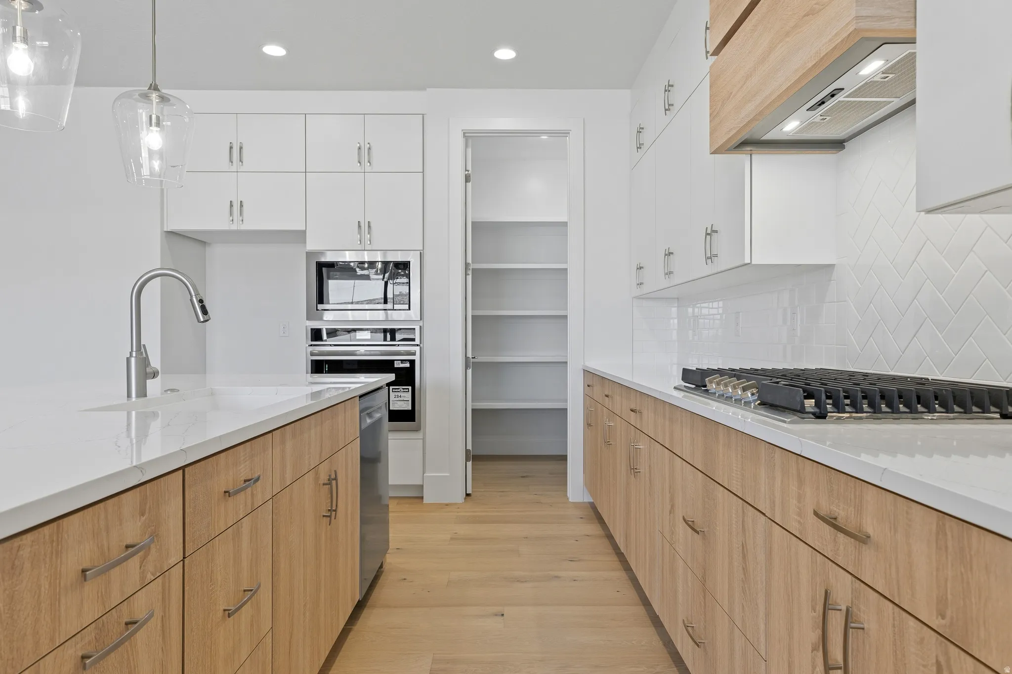 Contemporary kitchen featuring wood-finish lower cabinetry, white upper cabinetry, and a herringbone tile backsplash