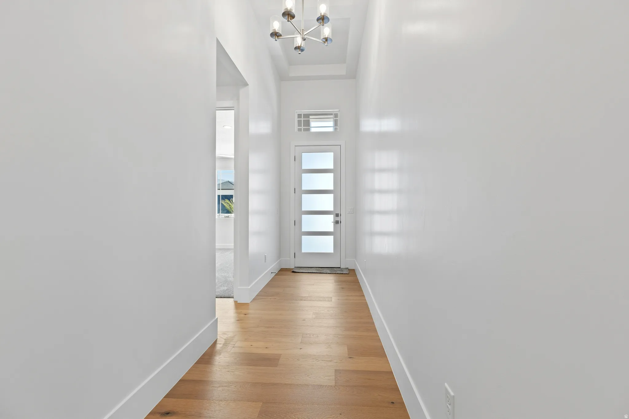 Entryway featuring wood-finish flooring, a modern chandelier, and a front door with frosted glass panels and an upper transom window