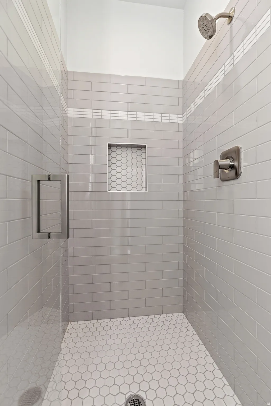 Shower stall featuring subway tile walls, a built-in niche with hexagonal tile, hexagonal mosaic floor tile, and brushed nickel fixtures