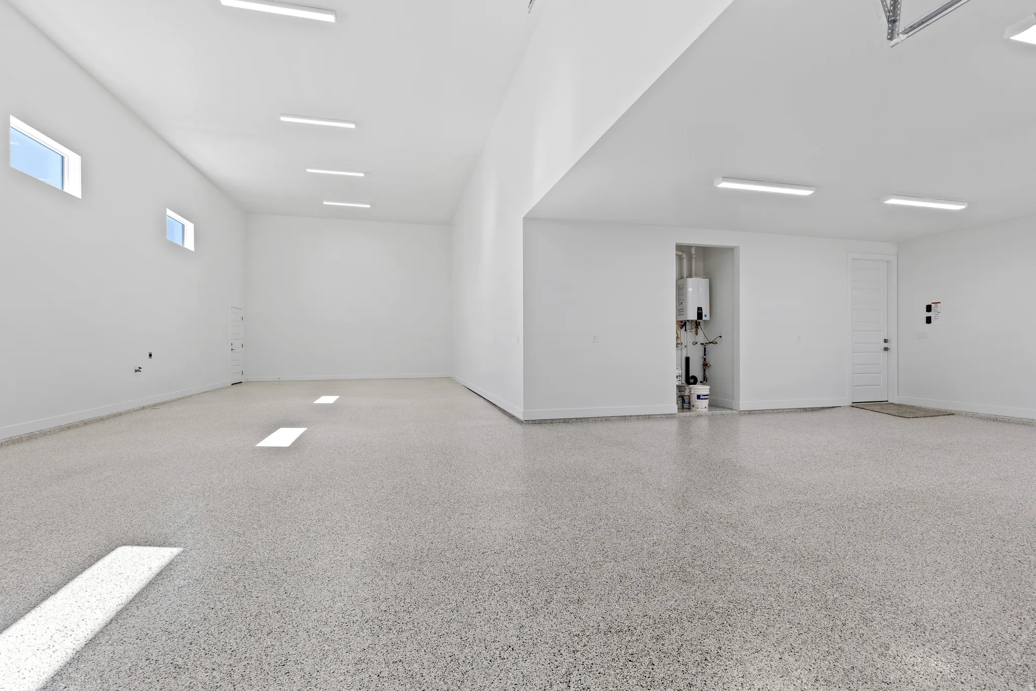 Spacious garage featuring a speckled epoxy floor, multiple linear ceiling lights, high ceilings, transom windows, and a dedicated utility alcove