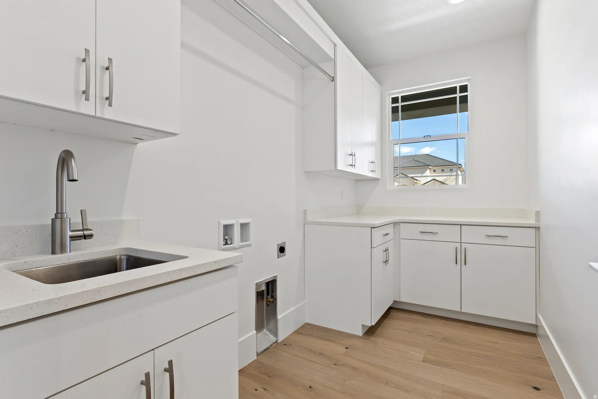 Utility room featuring white cabinetry, light countertops, wood-finish flooring, a stainless steel sink with a brushed nickel faucet, and a window for natural light