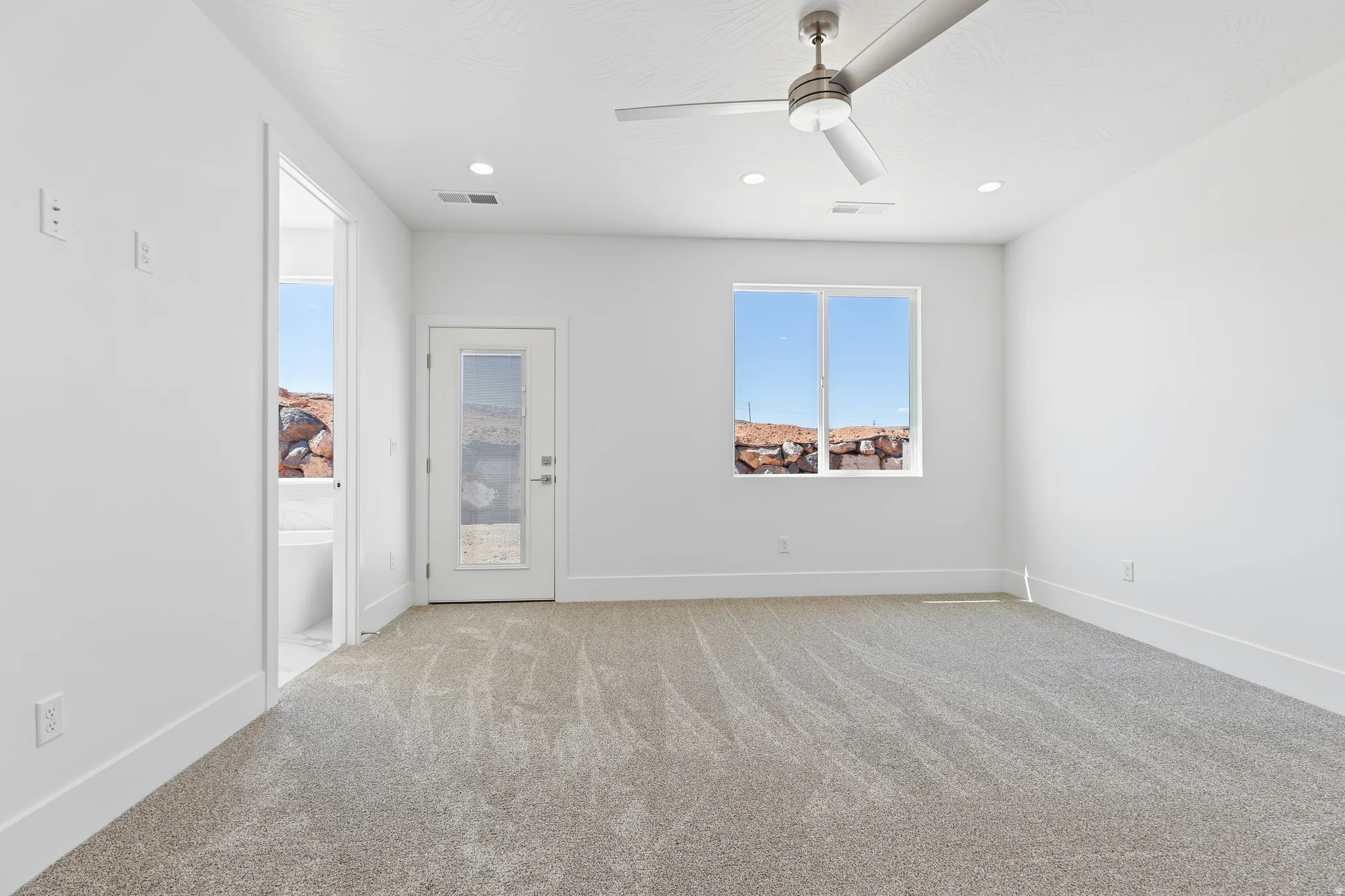 Spacious room featuring neutral carpeting, white walls, and a modern ceiling fan with integrated lighting