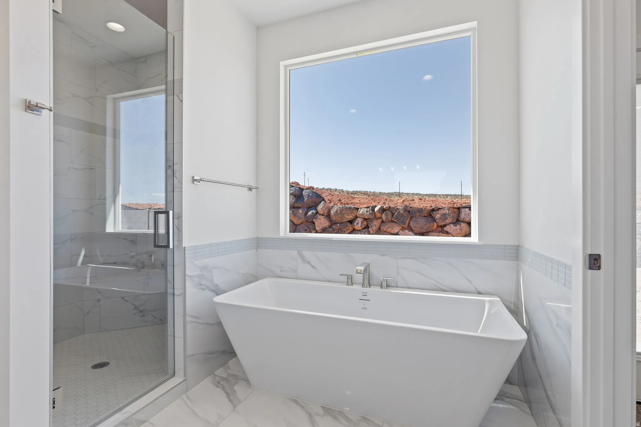 Freestanding soaking tub with brushed nickel fixtures, complemented by a large picture window