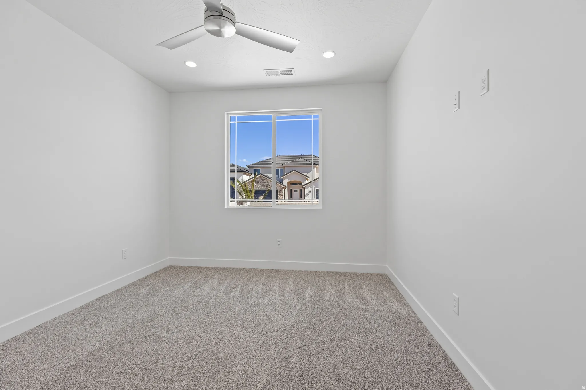 Bright interior space featuring a window, neutral-toned carpeting, white baseboards, recessed lighting, and a ceiling fan