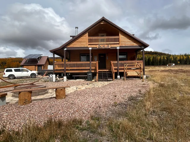 Log cabin exterior featuring a covered porch, second-story balcony, and a gravel-paved front yard with a fire pit area