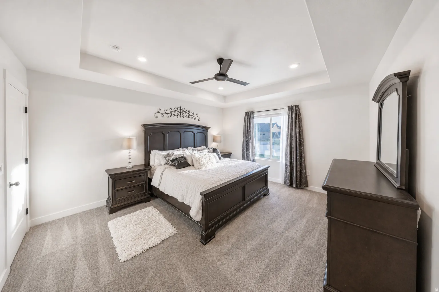 Spacious room featuring a tray ceiling with recessed lighting and a ceiling fan, patterned carpeting, and a window