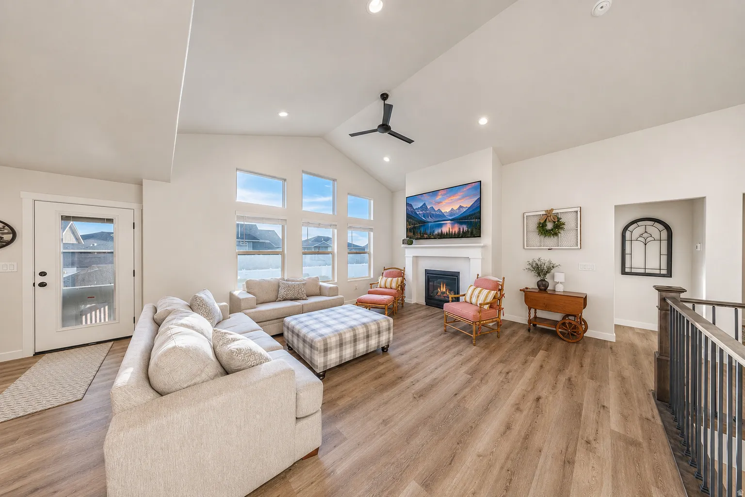 Vaulted ceiling great room featuring wood-finish flooring, a fireplace with a white mantel, and a wall of transom windows