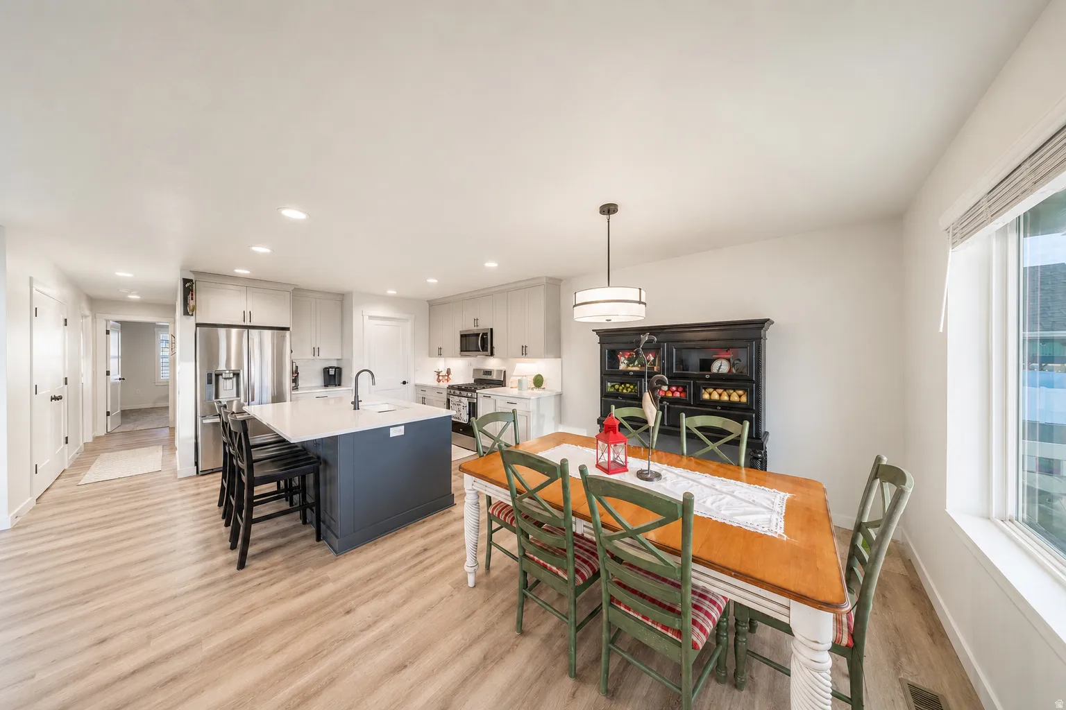 Open-concept kitchen and dining area featuring light wood-finish flooring, recessed lighting, a kitchen island with seating, a stainless steel refrigerator, and a window with blinds