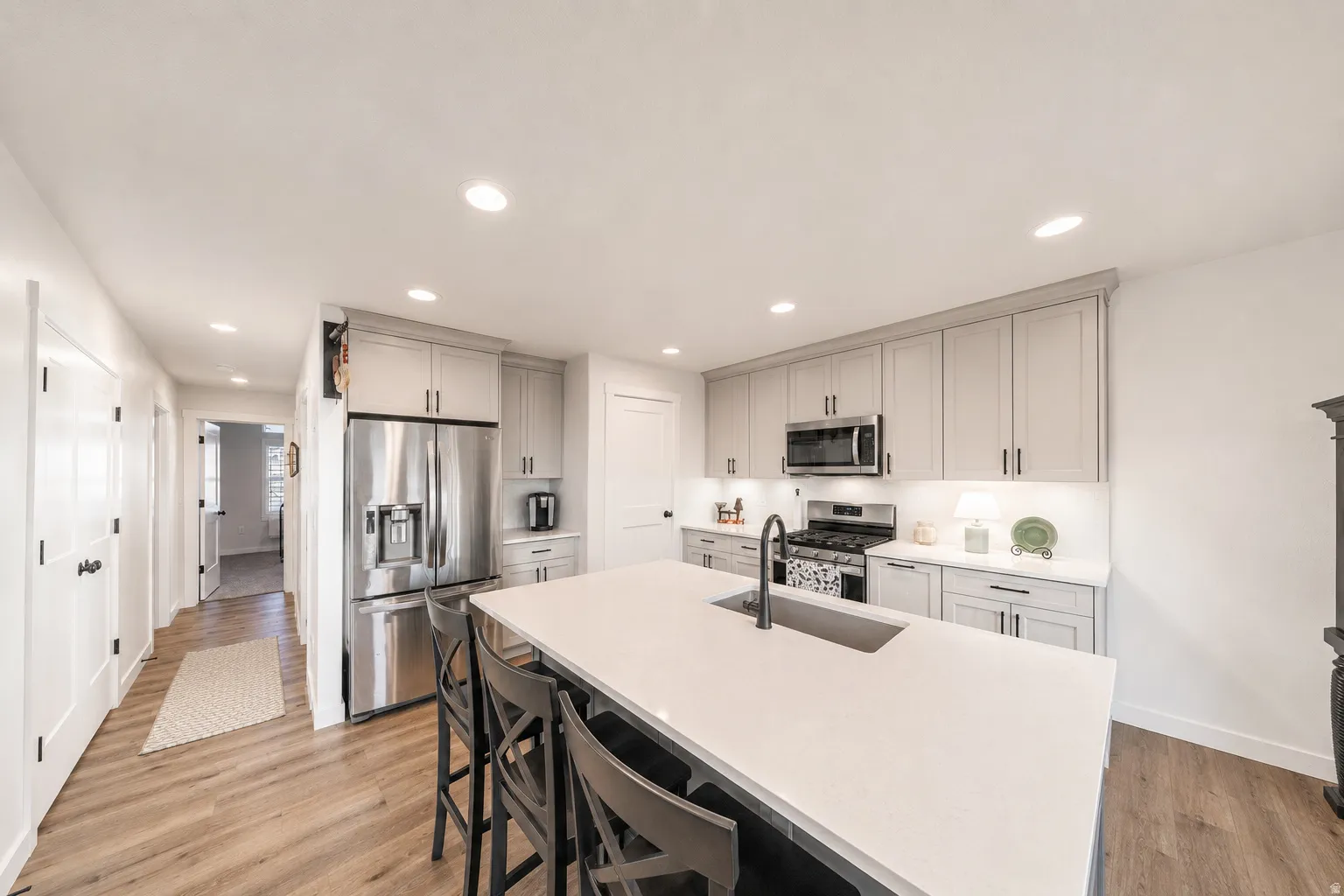 Kitchen featuring a large island with an integrated sink, light-colored cabinetry, stainless steel appliances, and recessed lighting