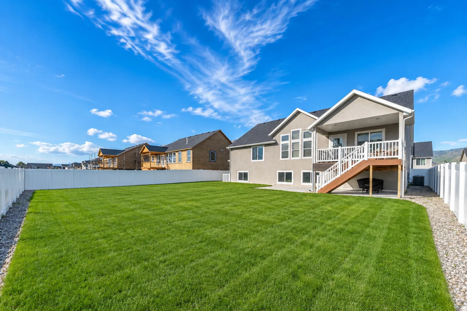 Expansive fenced backyard with a manicured lawn, gravel perimeter, and a two-story exterior featuring a covered patio and an upper-level deck with white railings