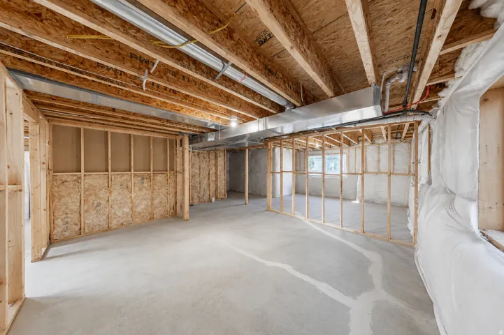 Unfinished basement featuring concrete flooring, exposed wood framing, and overhead ductwork