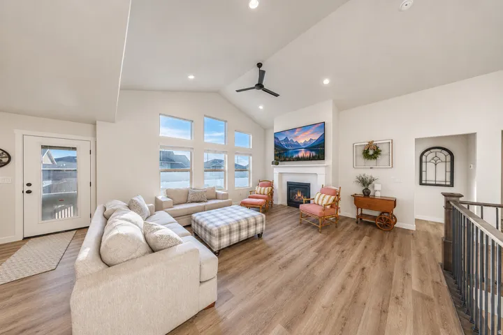 Vaulted ceiling great room featuring wood-finish flooring, a fireplace with a white mantel, and a wall of transom windows