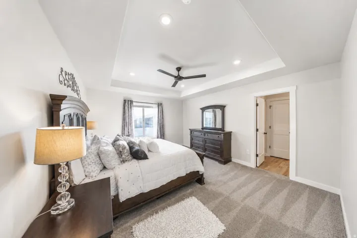 Primary bedroom featuring a tray ceiling with recessed lighting and a ceiling fan, carpet flooring, and a window with blinds