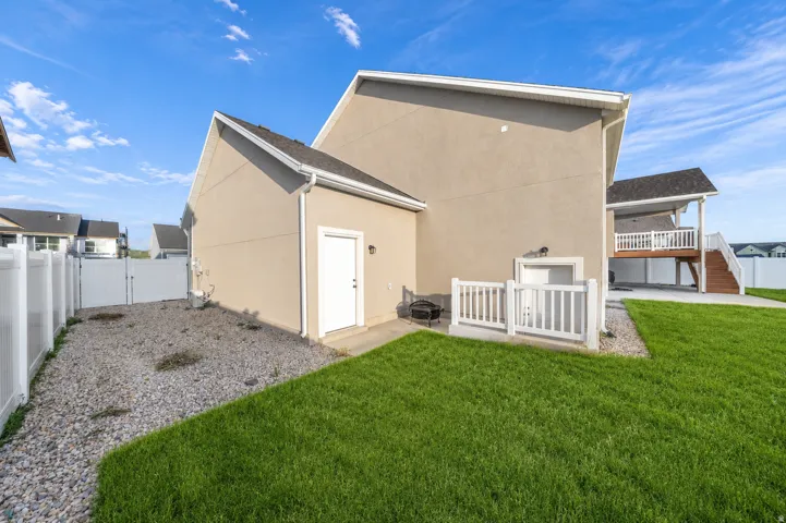 Expansive backyard featuring a separate basement entrance, manicured lawn, gravel landscaping, and a full privacy fence