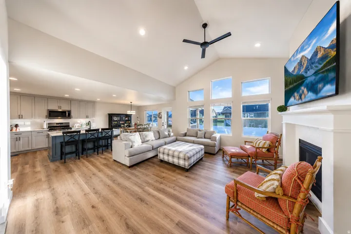 Open-concept living space featuring wood-finish flooring, a vaulted ceiling with a ceiling fan, and a fireplace with a white mantel
