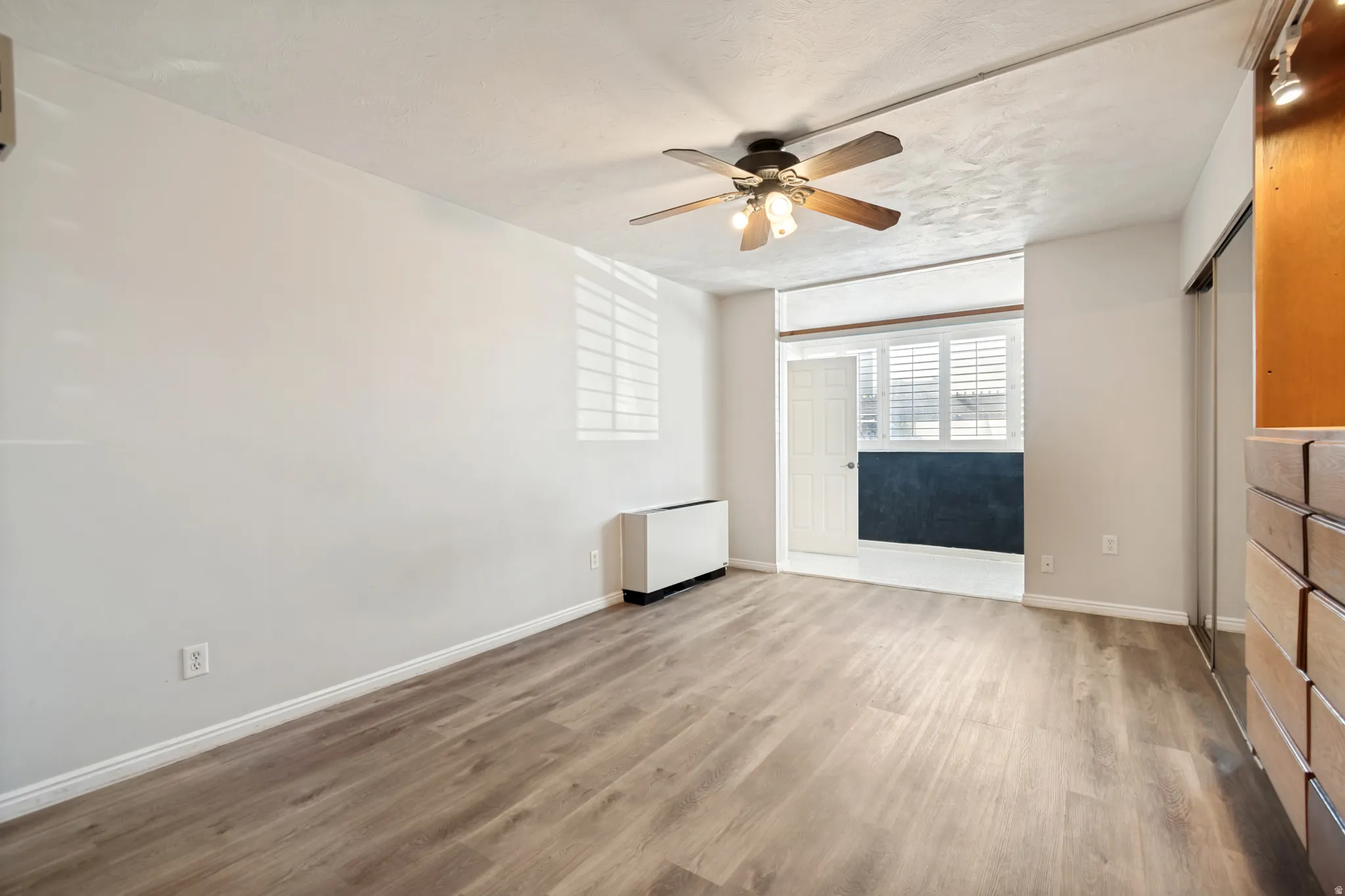 Spacious room featuring wood-finish flooring and a ceiling fan with integrated lighting