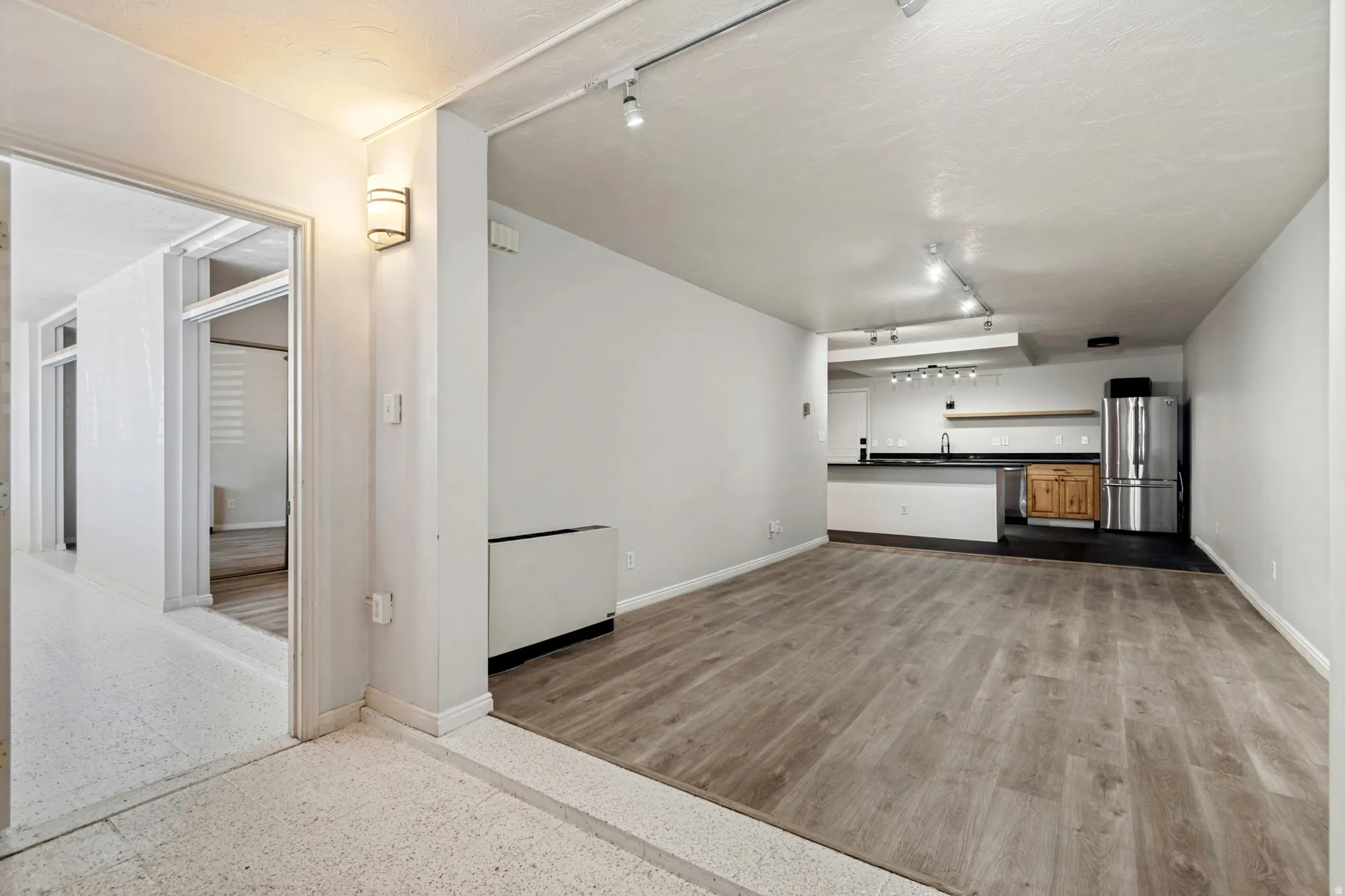 Open concept living space featuring wood-finish flooring, track lighting, and a kitchen area with a stainless steel refrigerator, dark countertops, and wood cabinetry