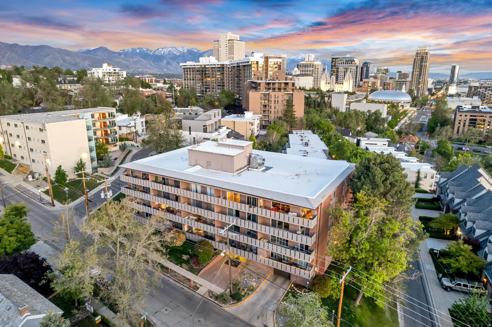 Contemporary multi-story building featuring individual balconies and surrounding mature trees