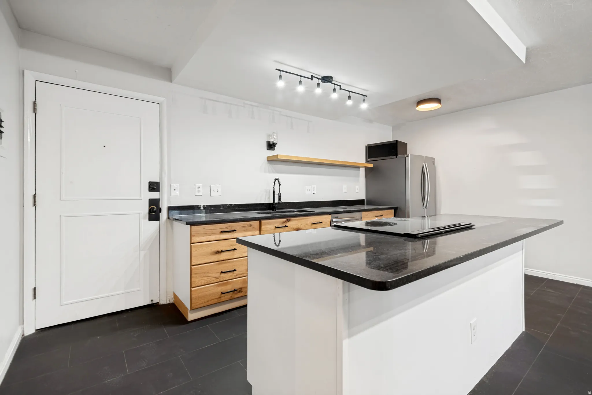 Kitchen featuring an island with an integrated cooktop, dark countertop, and perimeter cabinetry with natural wood-finish drawers