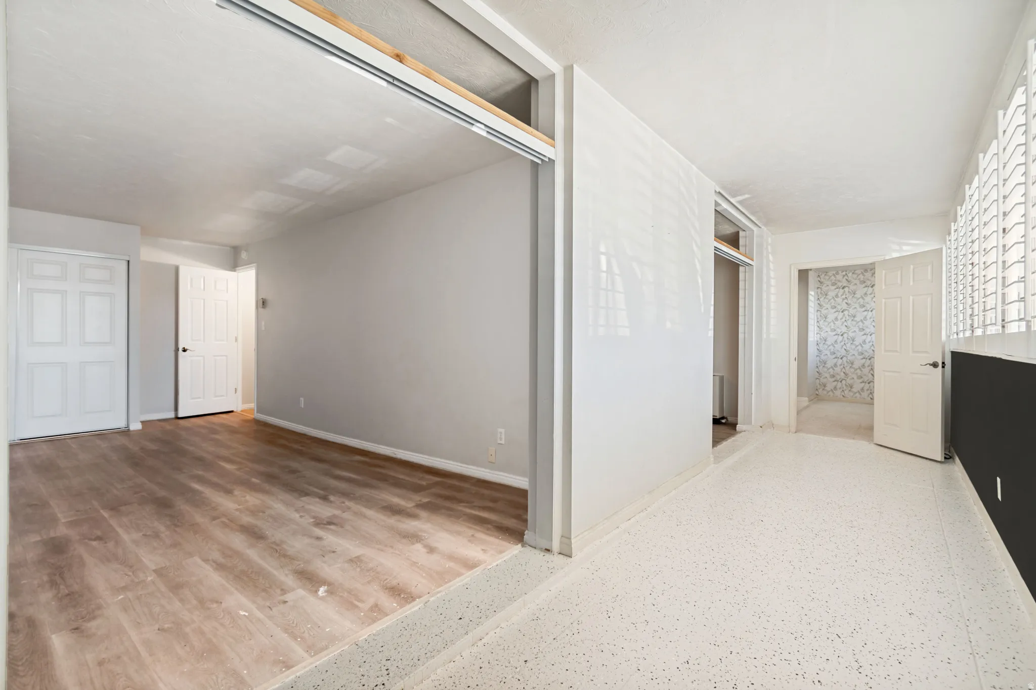 Multi-level interior featuring wood-finish flooring, white doors, and a partial wall with horizontal louvered windows