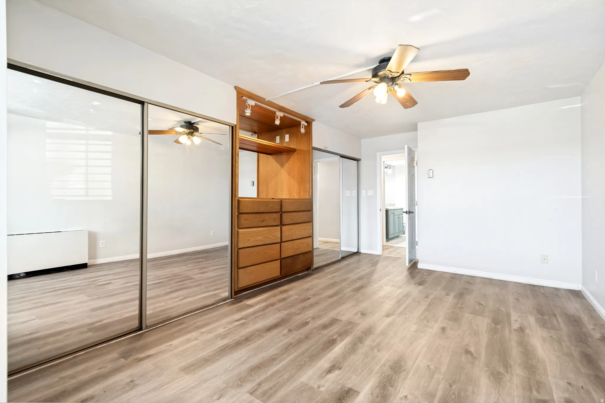 Spacious interior featuring wood-finish flooring, a built-in wood-tone storage unit with drawers and shelving, and track lighting