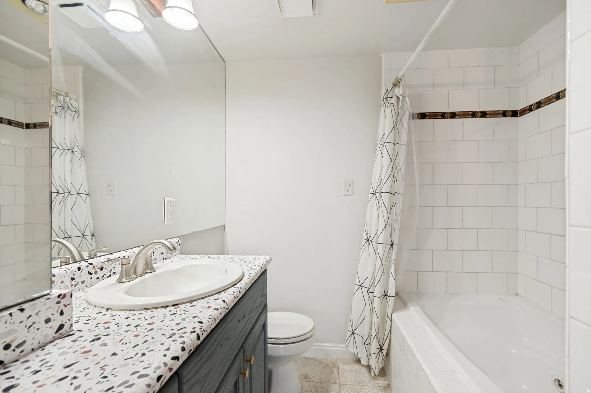 Bathroom featuring a white subway tile shower, a built-in tub, and a vanity with a terrazzo-style countertop