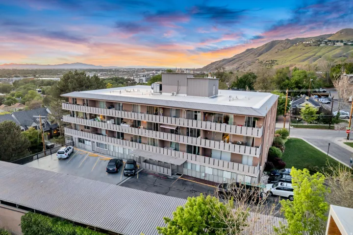 Multi-story building featuring individual balconies, a covered parking structure, and an additional surface parking area
